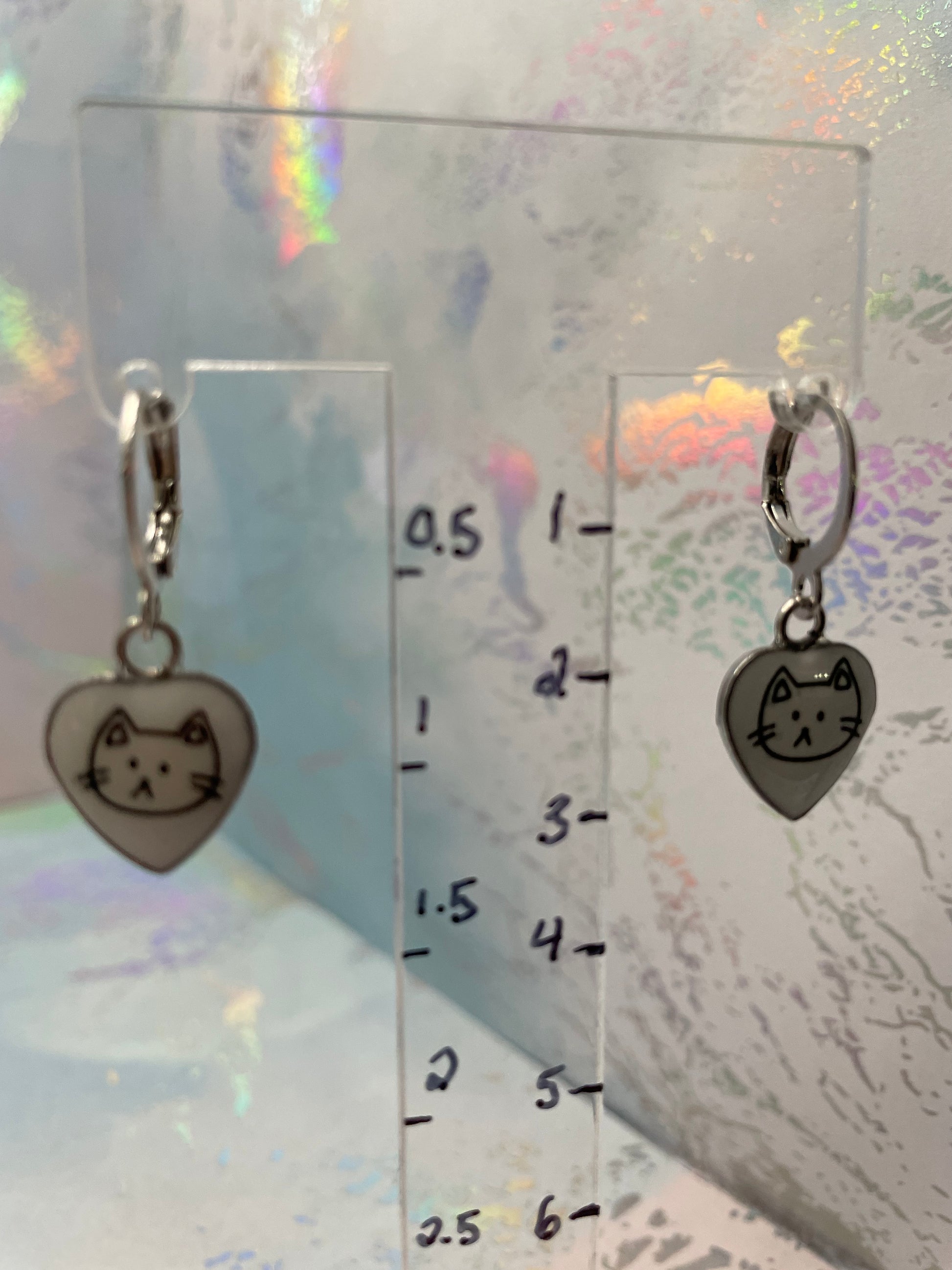 Cat-shaped earrings with a clear ruler for scale on a textured background