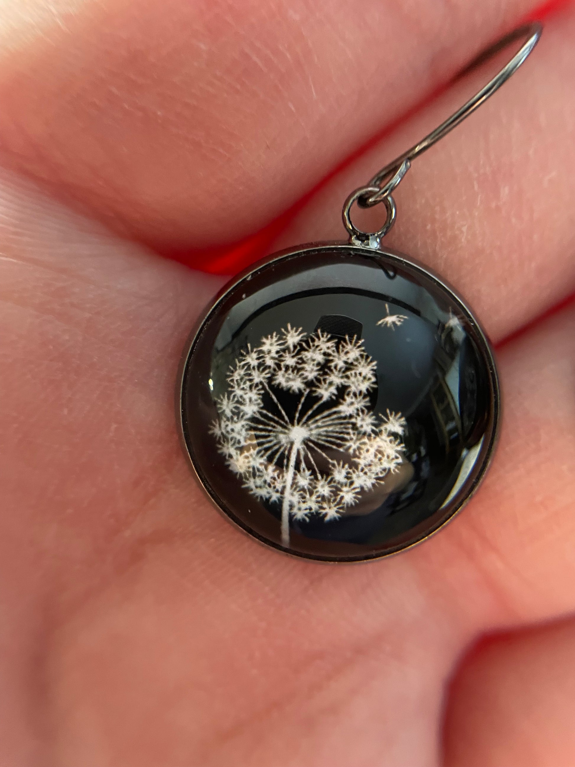 Close-up of a black earring with a floral design held between fingers.