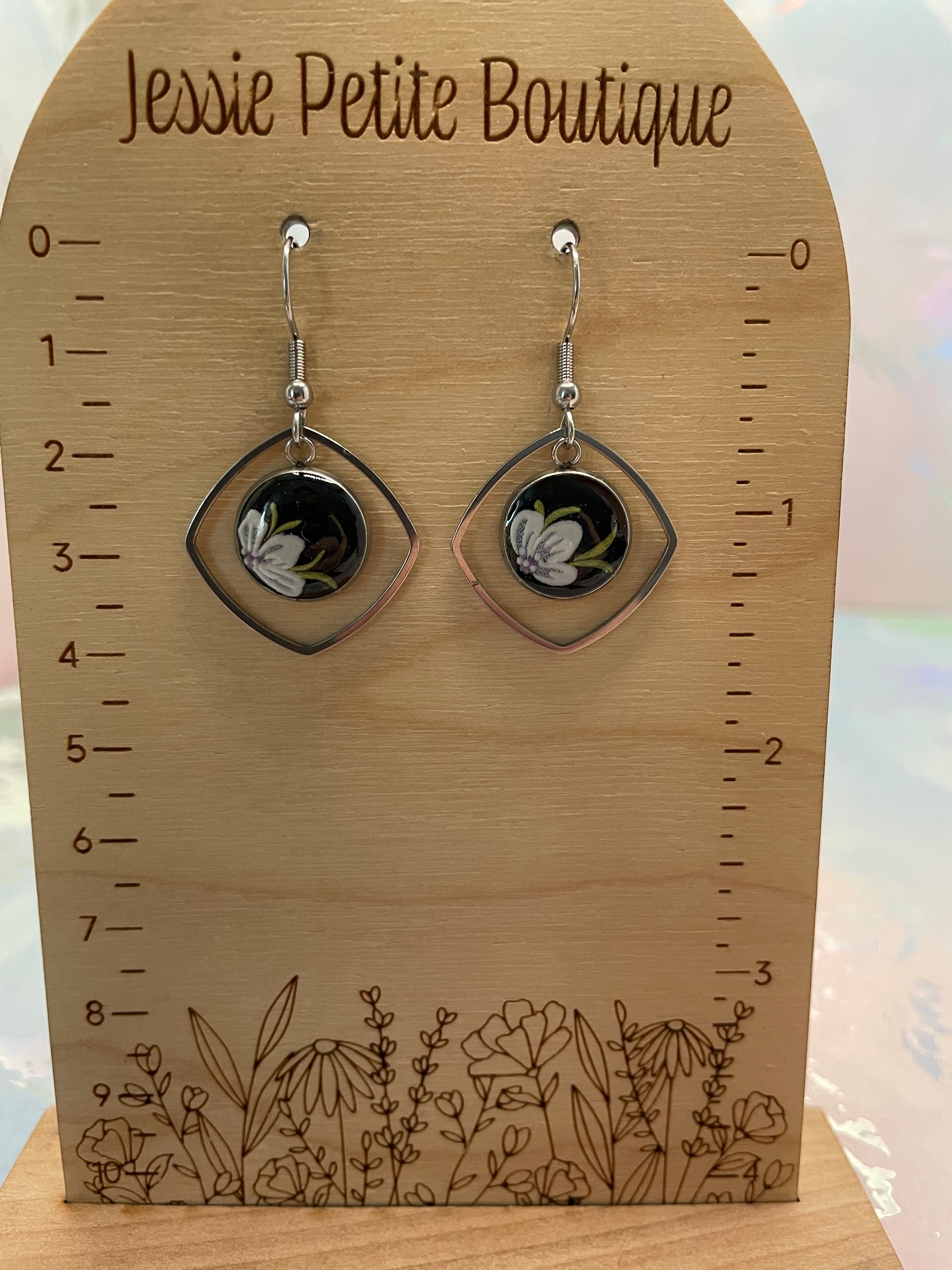 Pair of earrings on a wooden display card with floral designs and measurements, branded 'Jessie Petite Boutique'.