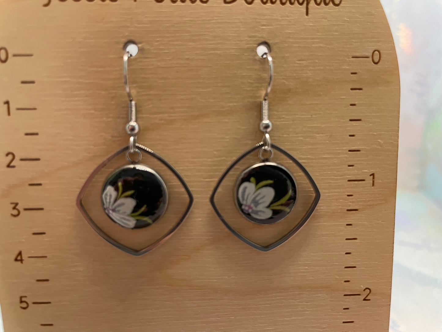Pair of earrings on a wooden display card with measurement scale.