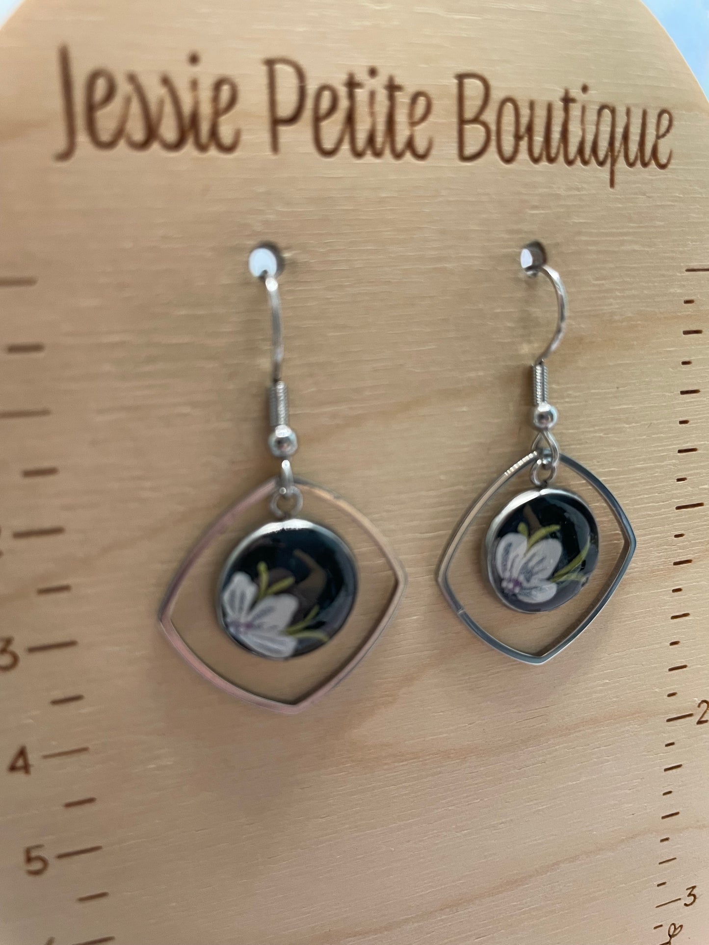 Pair of earrings on a wooden surface with 'Jessie Petite Boutique' branding.