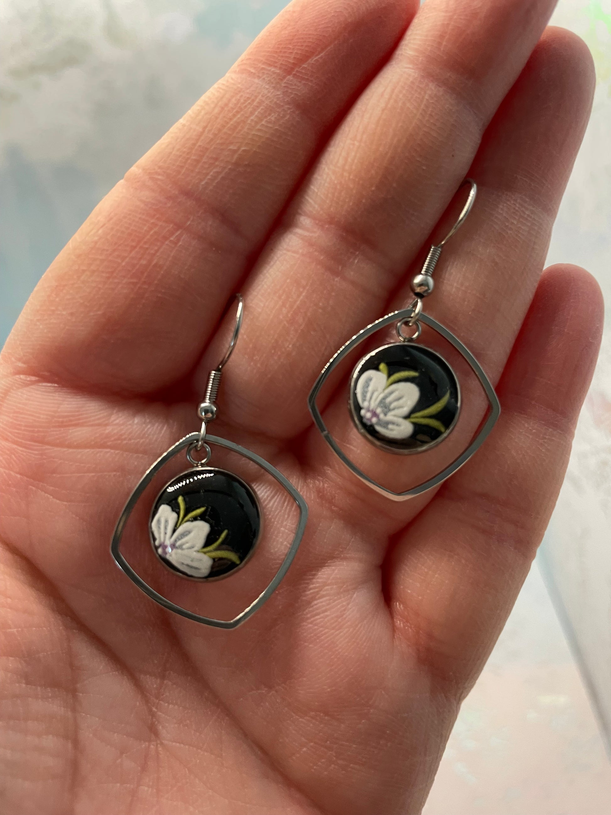 Silver earrings with floral design held in a hand against a light background