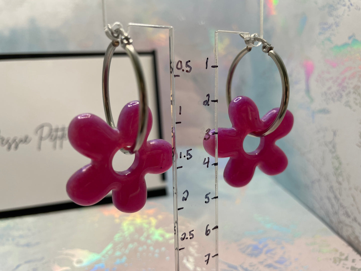 Pink flower-shaped earrings on a clear stand with measurement scale.