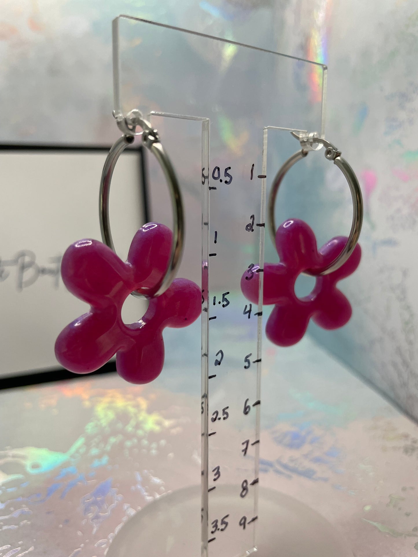 Pink flower-shaped earrings on a transparent stand with measurement scale.