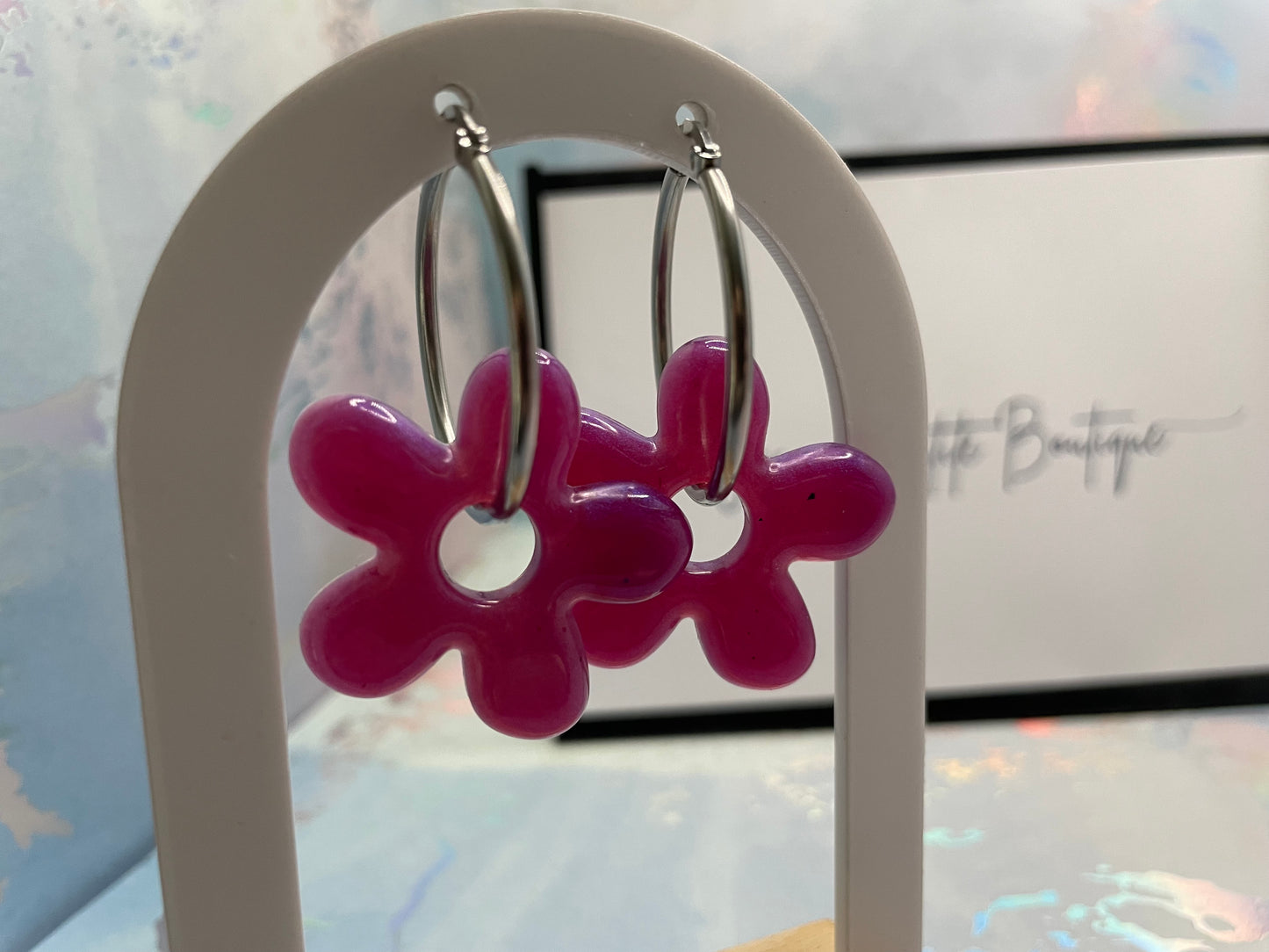Pink flower-shaped earrings on a white stand with a blurred background