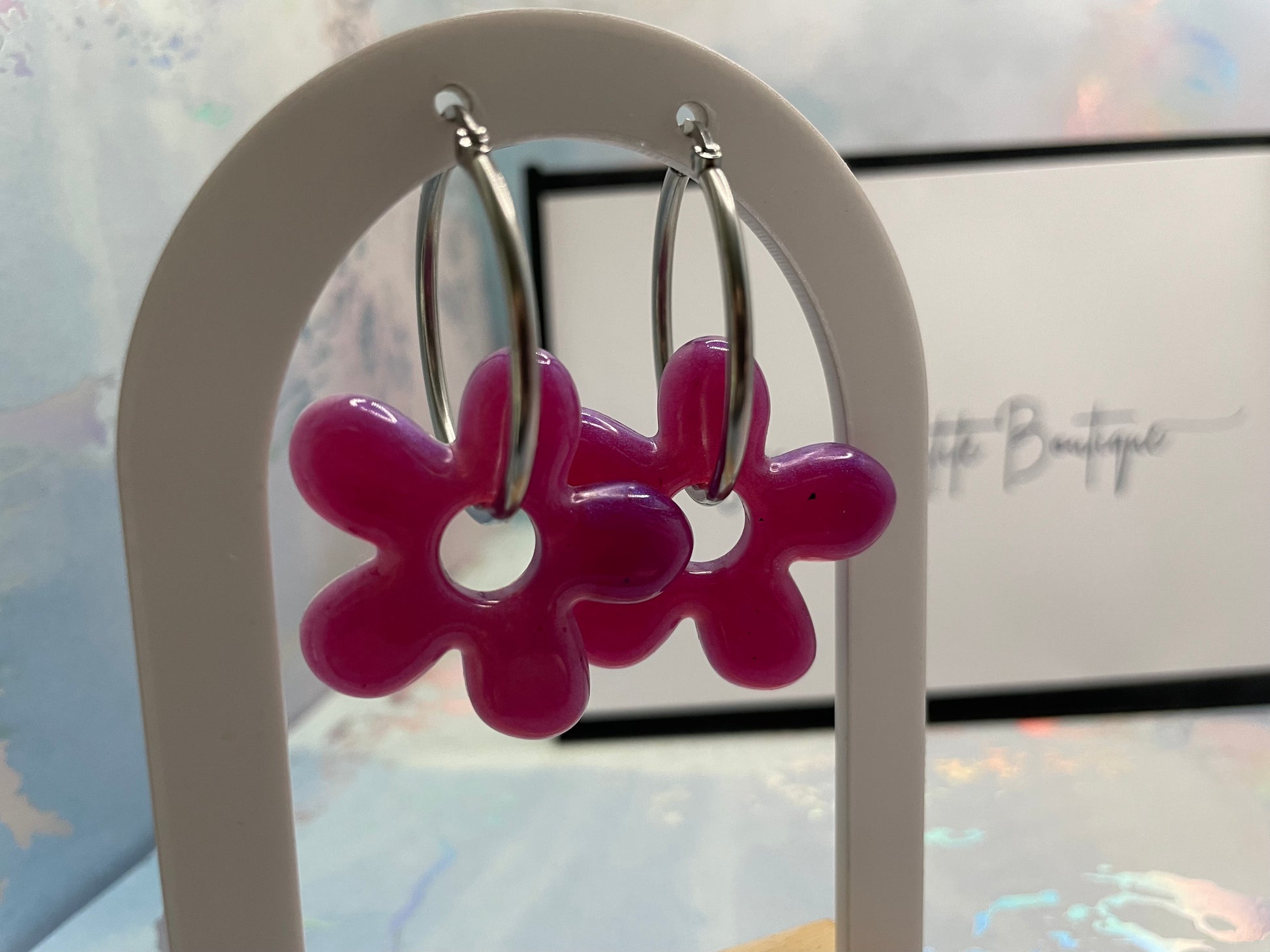 Pink flower-shaped earrings on a white stand with a blurred background