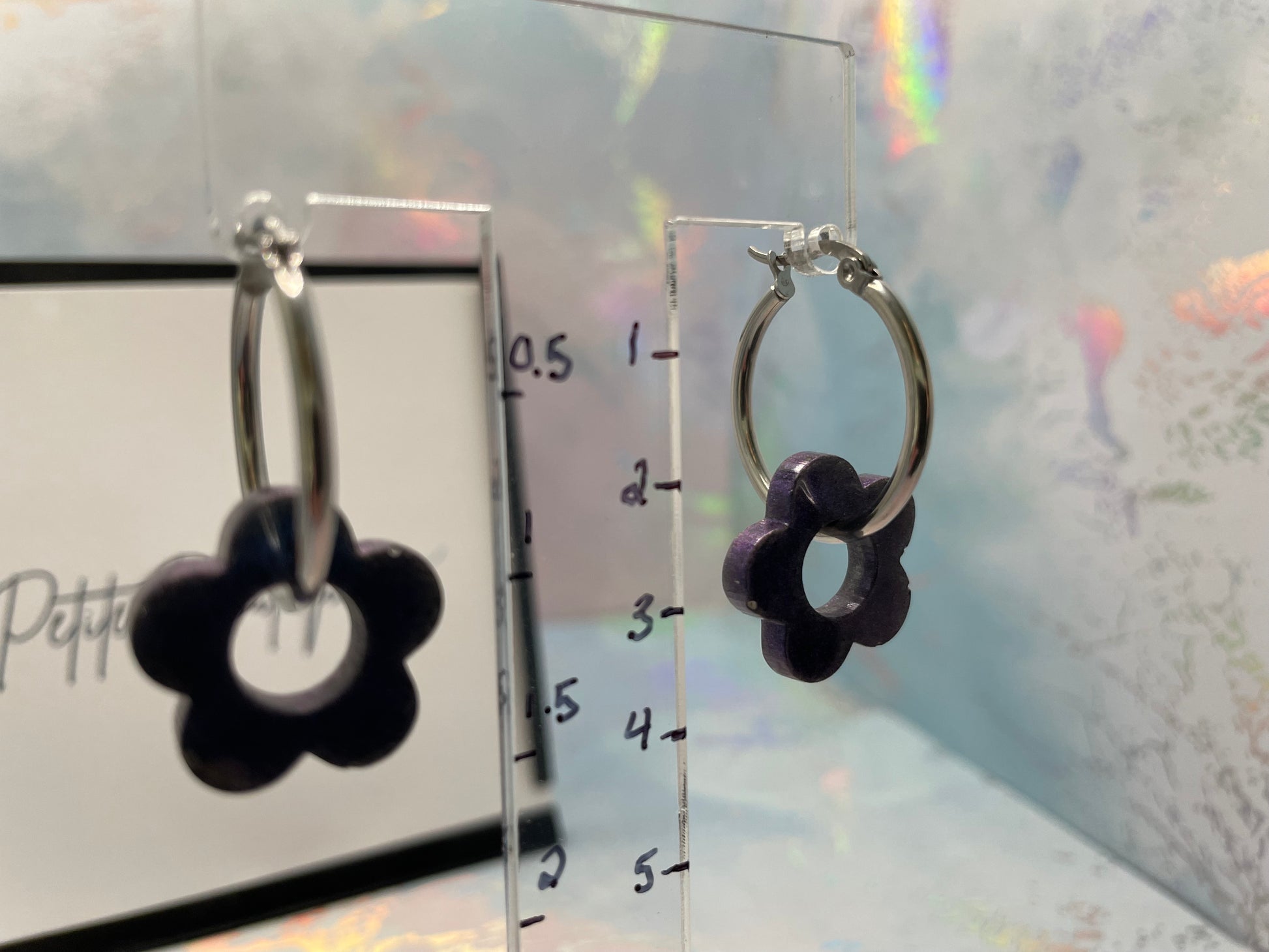 BLUE flower-shaped earrings on a clear stand with measurement scale against a light background