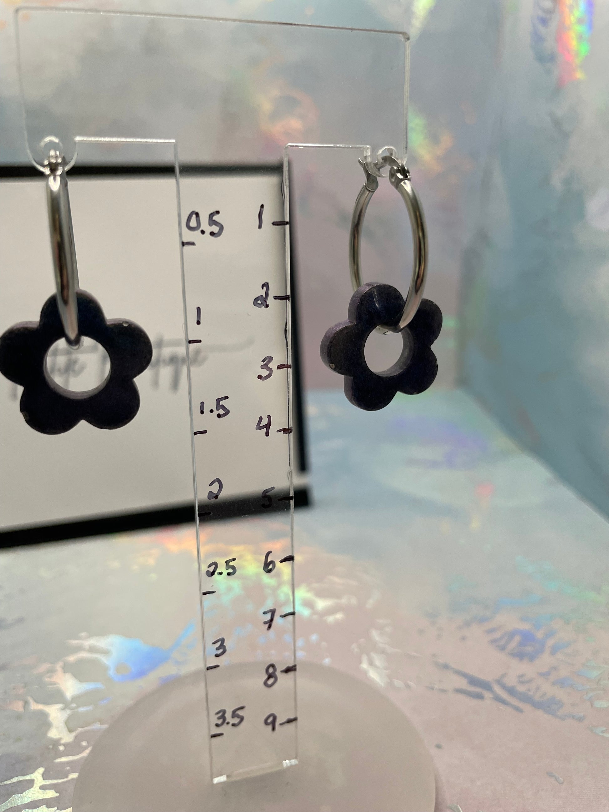 BLUE  flower-shaped earrings on a transparent stand with a ruler for scale.