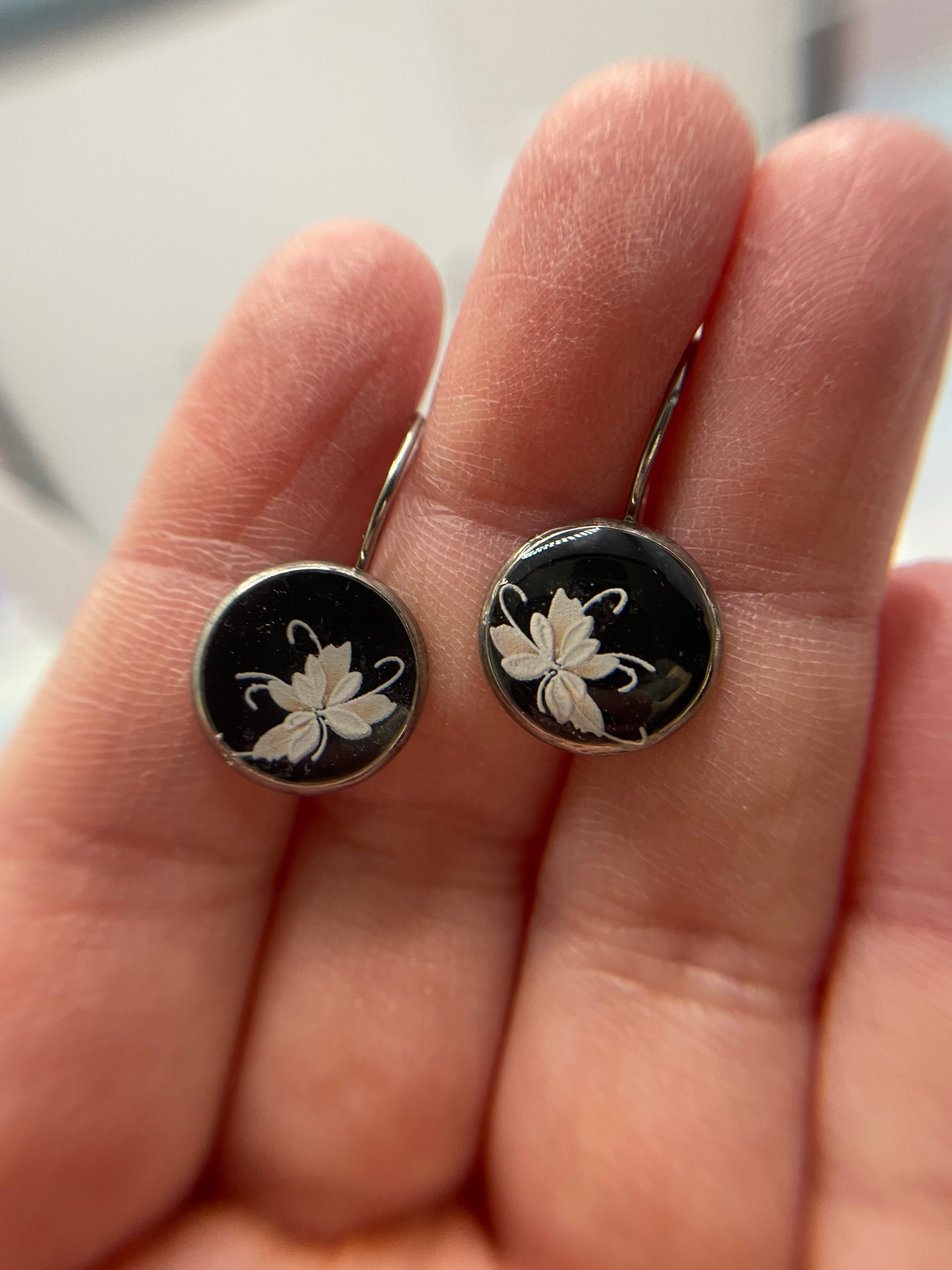 Black earrings with white floral designs held between fingers against a neutral background