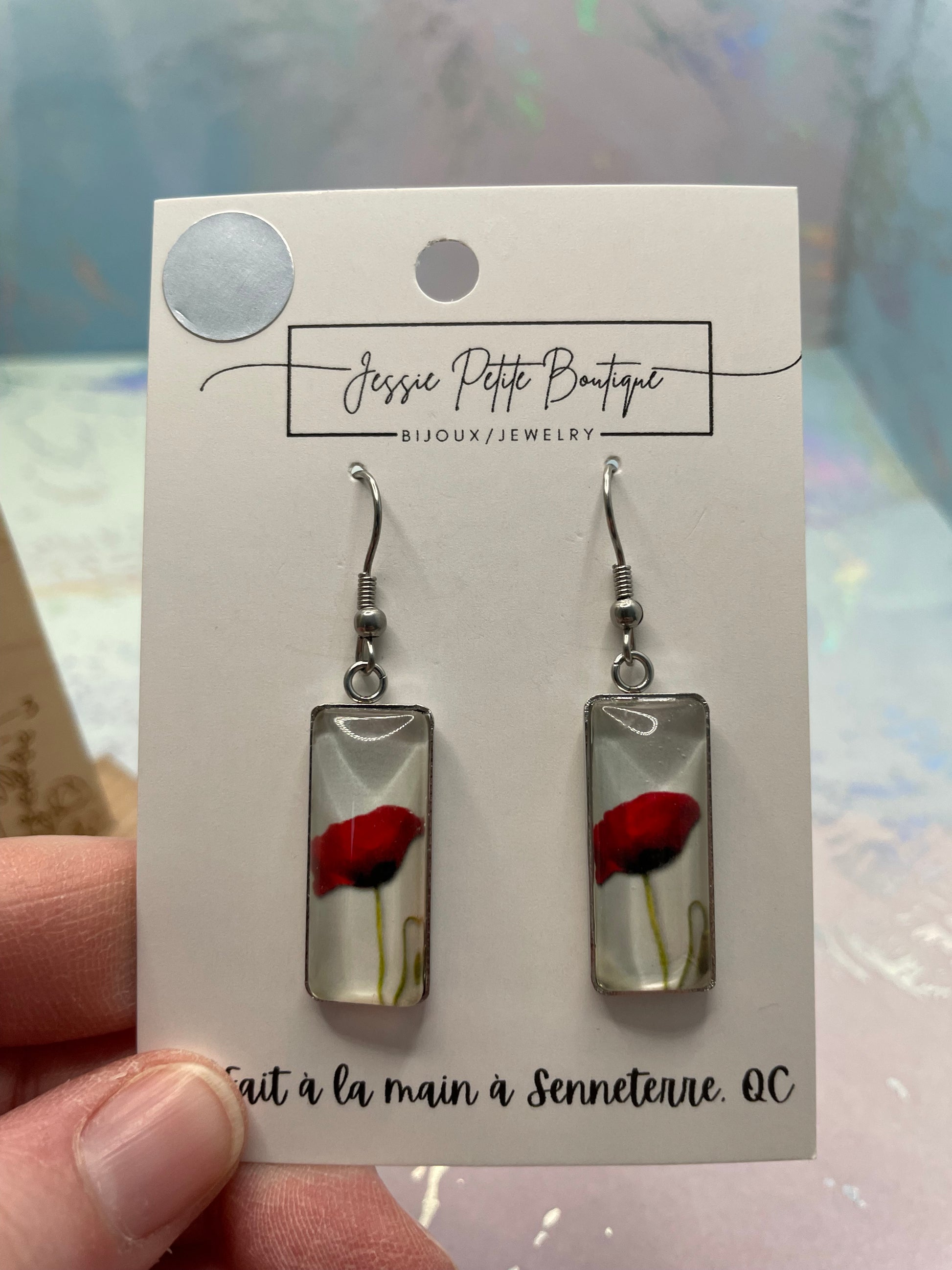 Pair of earrings on a card held by a hand with a blurred background