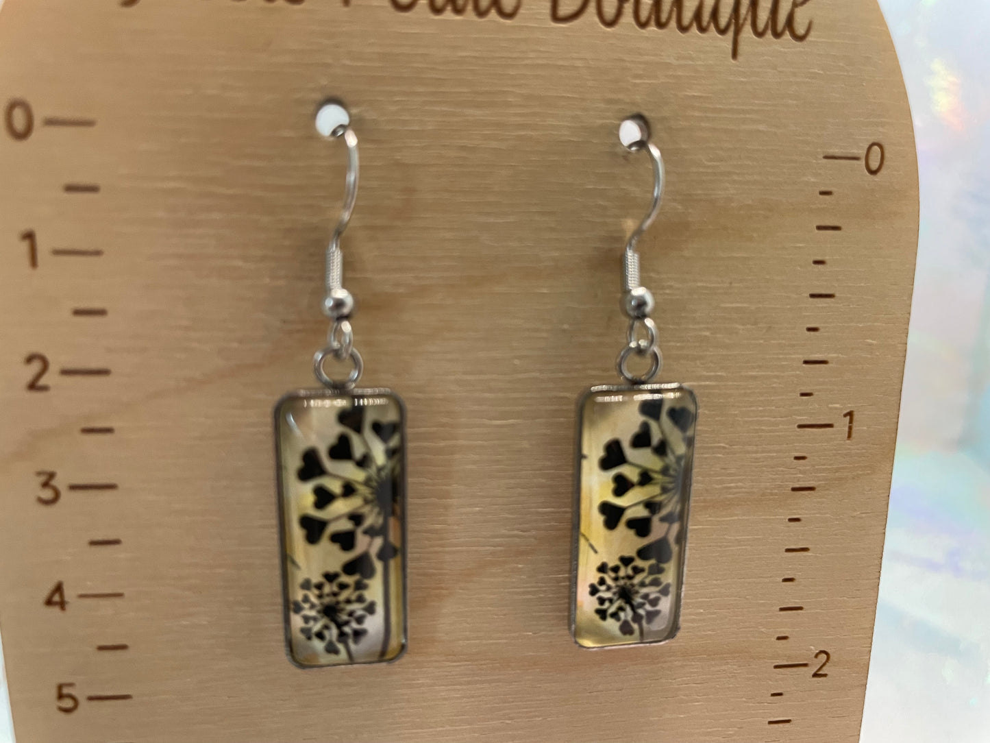 Pair of earrings with floral design on a wooden display card with measurements.