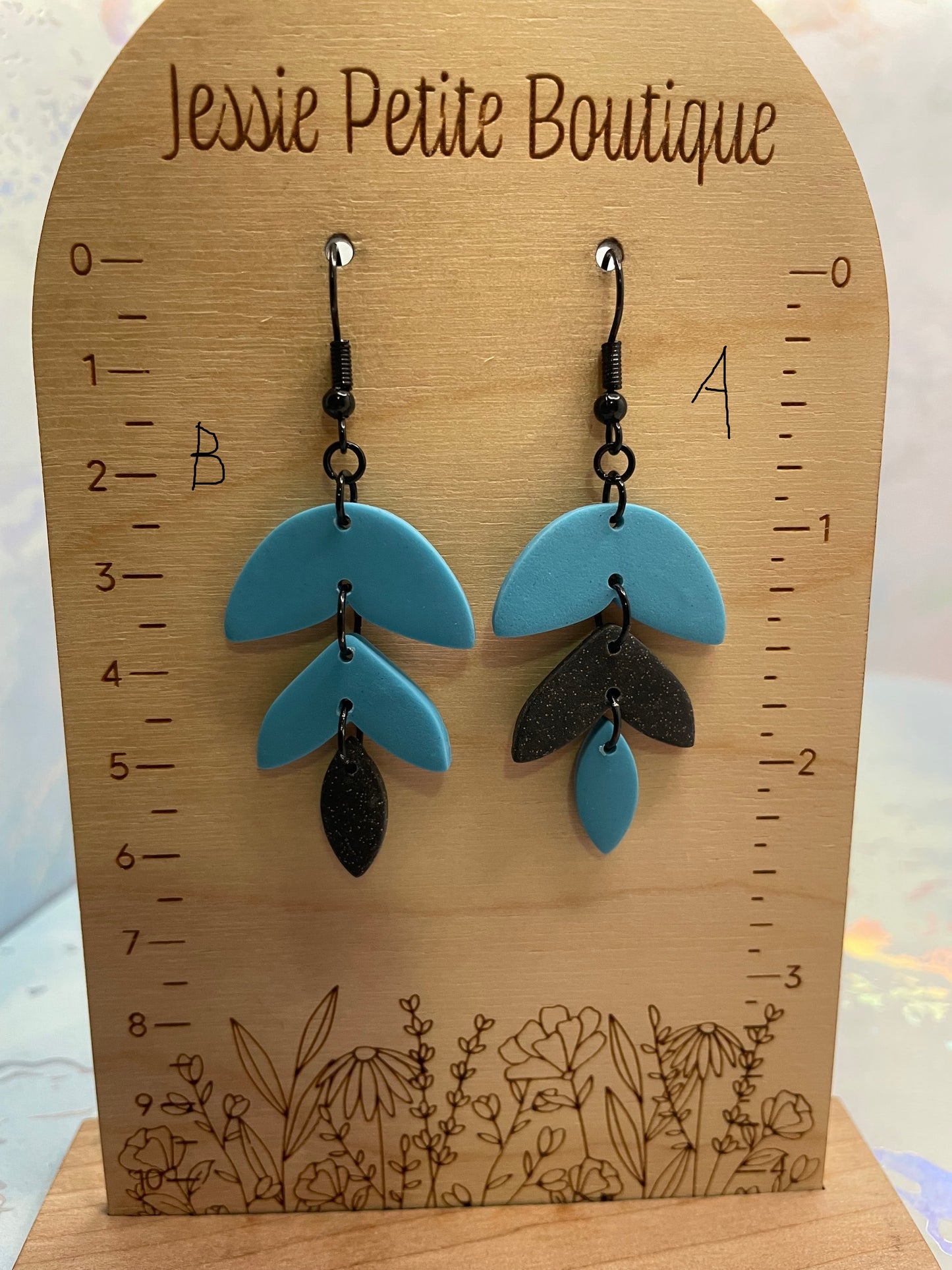 Blue alba earrings on a wooden measuring board with floral designs, branded 'Jessie Petite Boutique'.