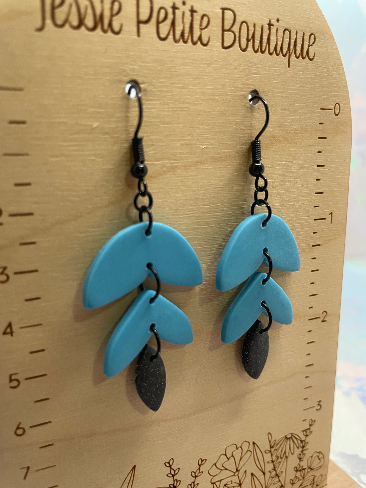 Blue earrings on a wooden surface with a ruler for scale.