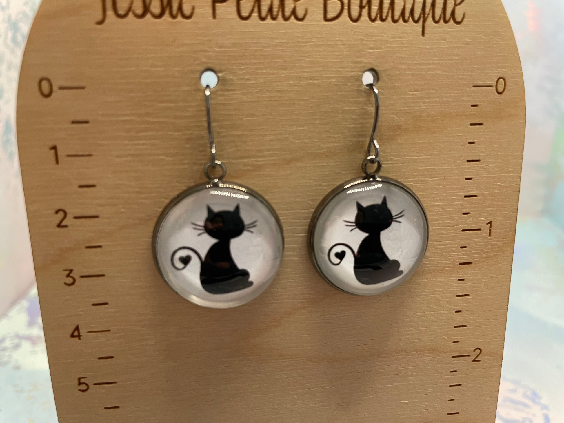 Cat-shaped earrings on a wooden display card with measurement scale.