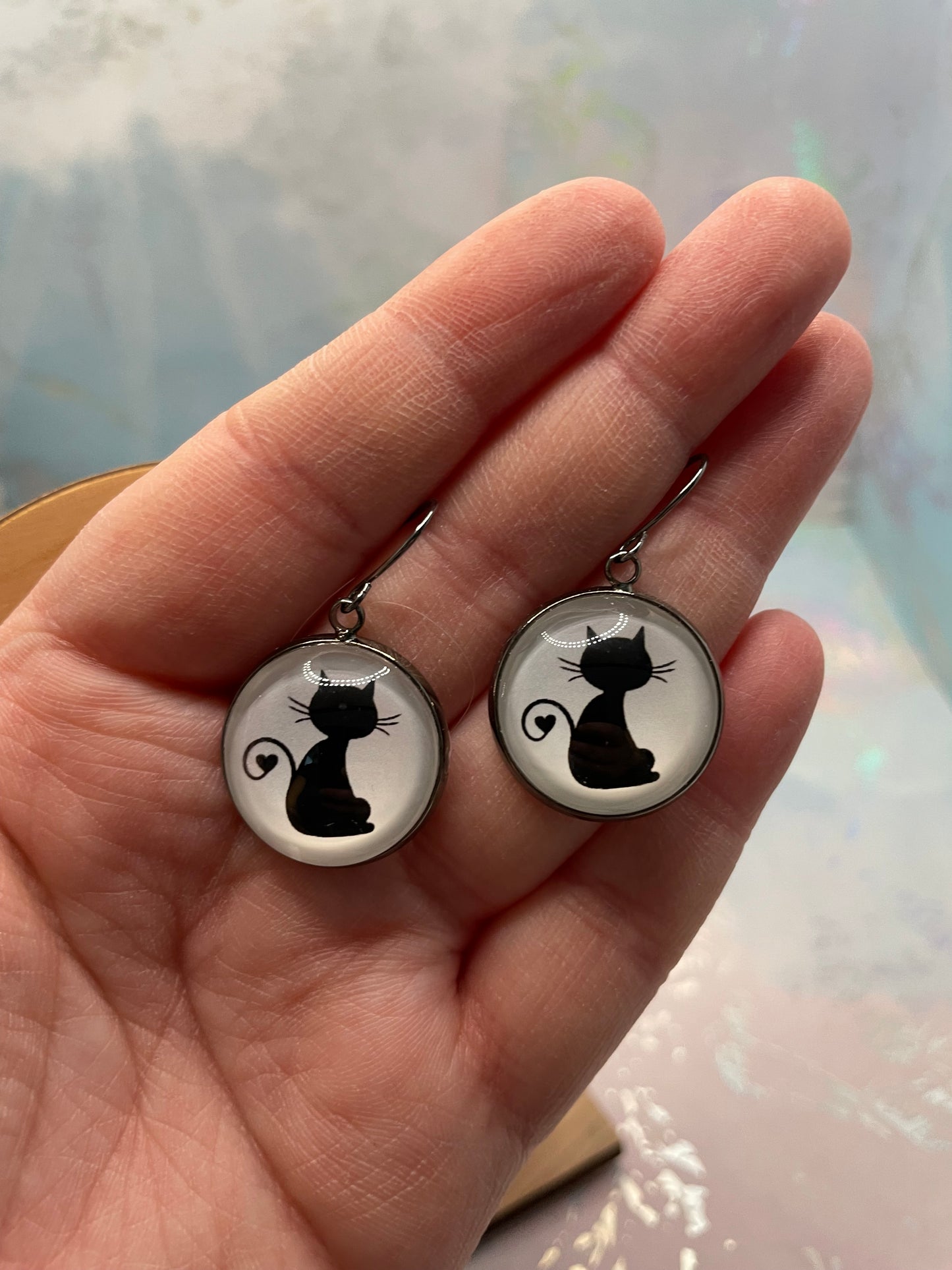 Two gun-metal earrings with black cat designs held in a hand against a light background.