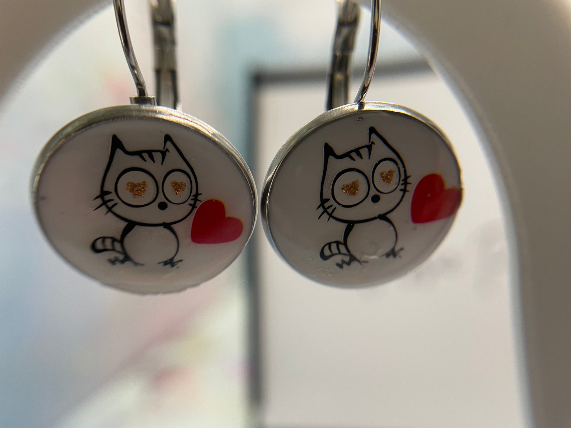Pair of earrings with cat illustration and red heart on a white background