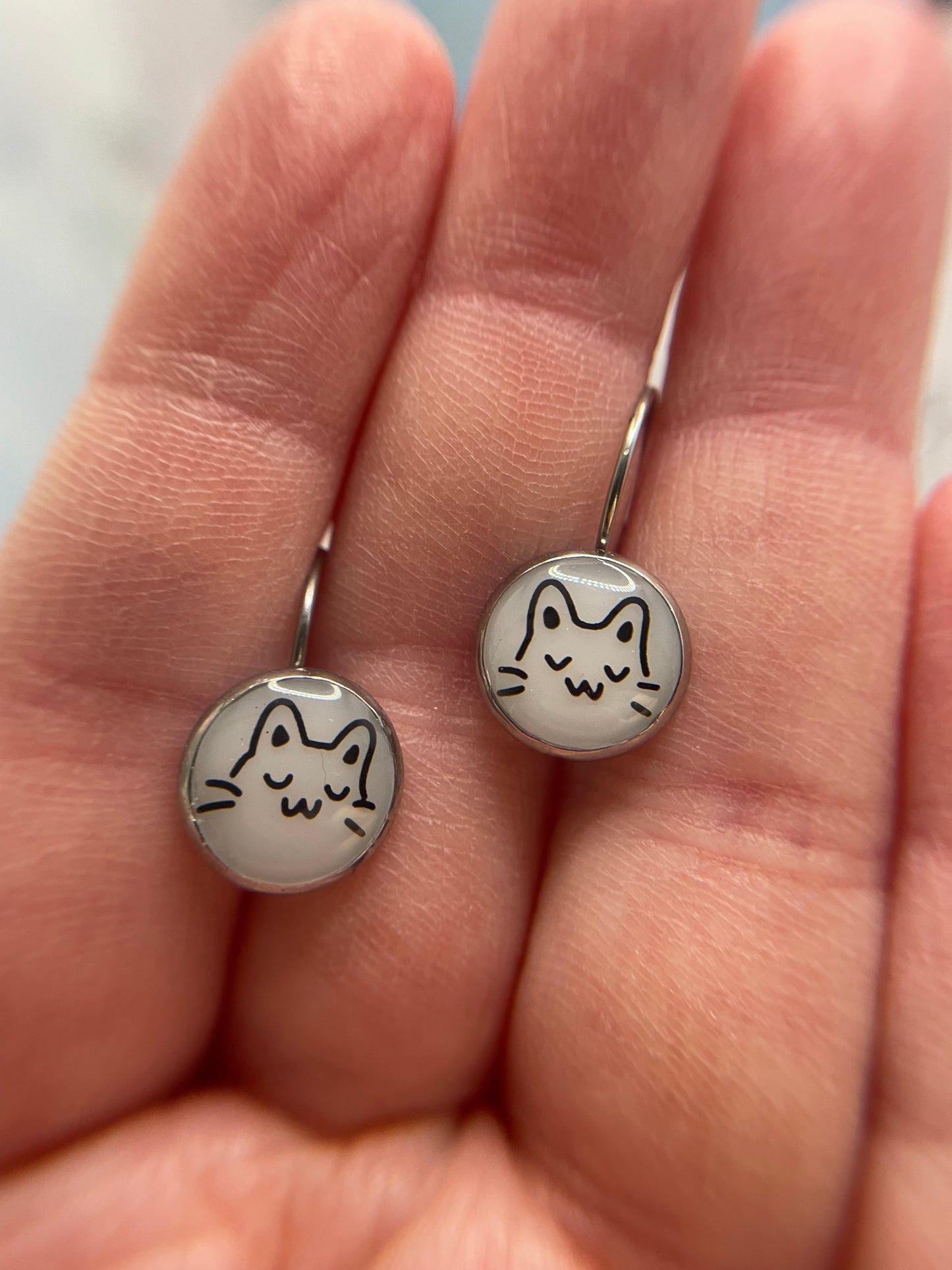 Silver earrings with cat designs held in a hand