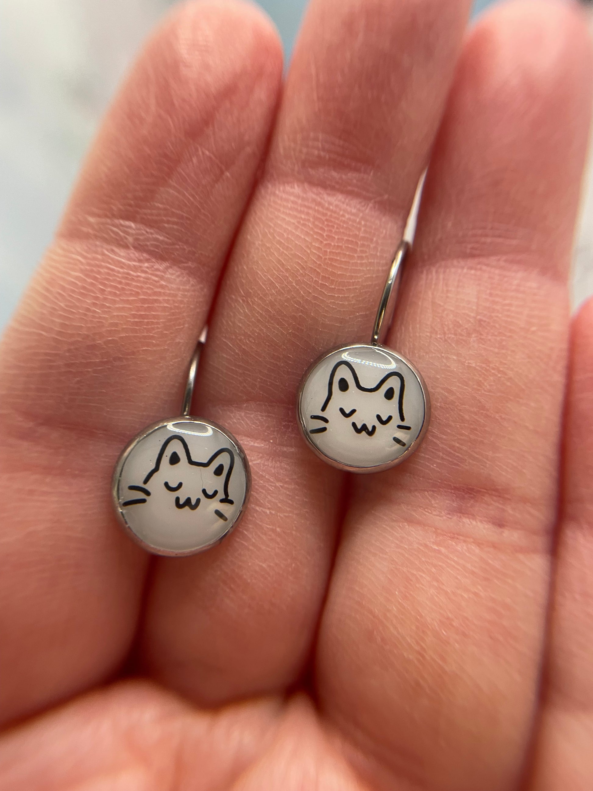 Silver earrings with cat designs held in a hand