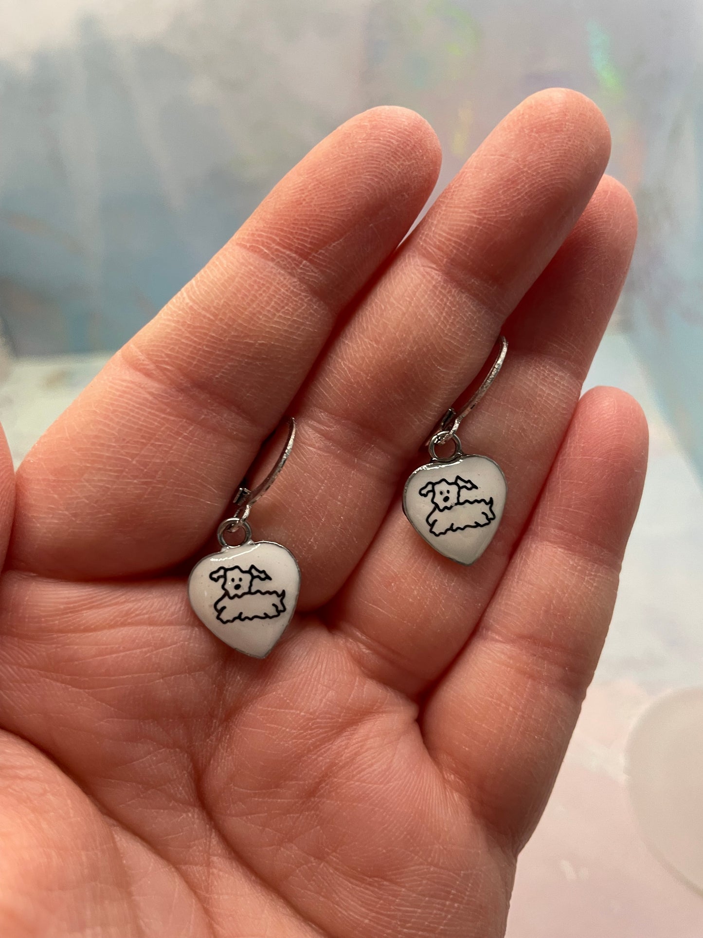 Heart-shaped earrings with dog prints held in a hand against a blurred background