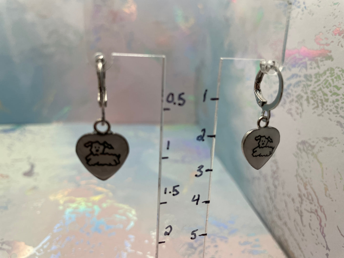 Silver heart-shaped earrings with engraved designs on a clear ruler for scale.