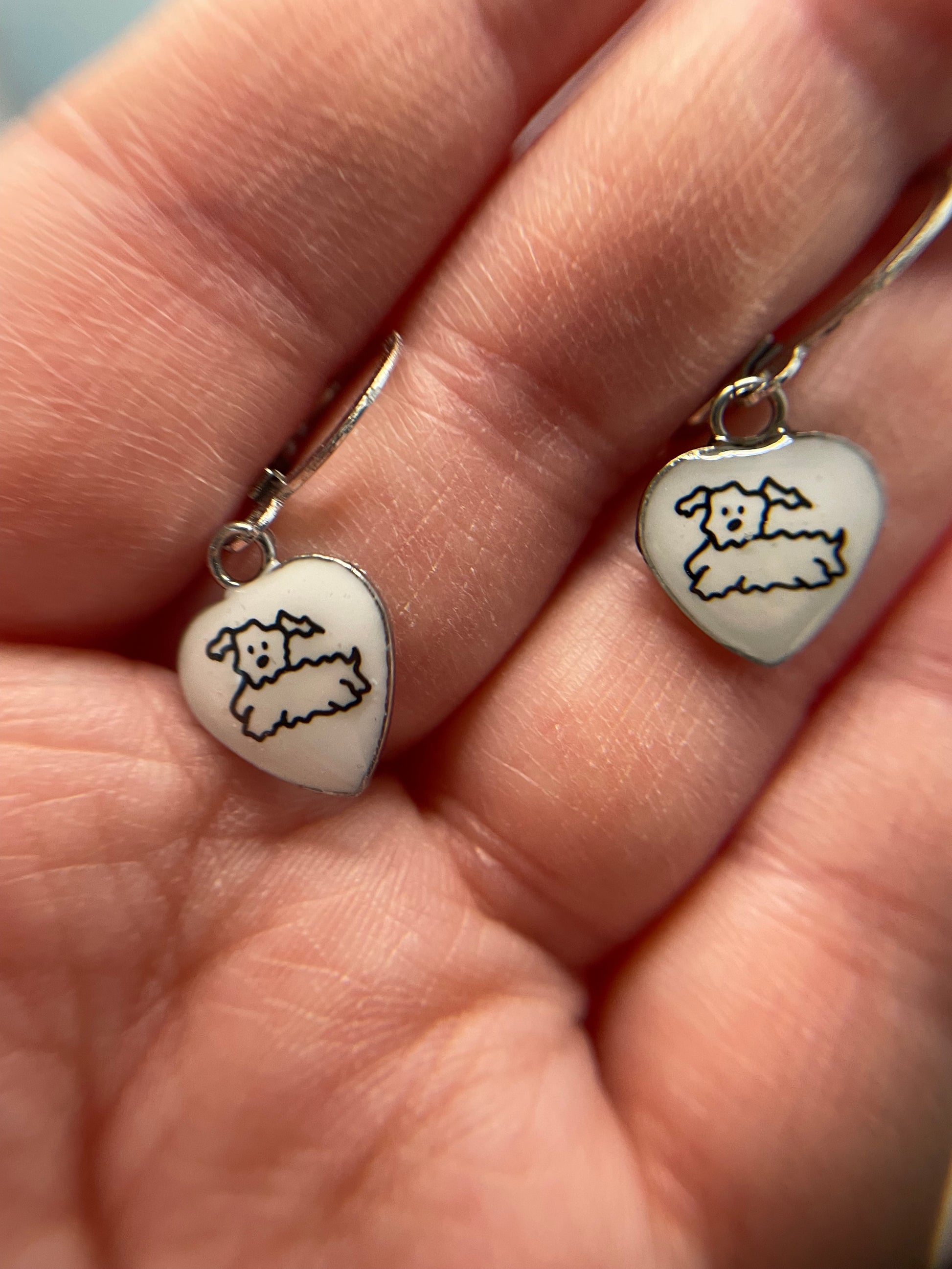 Heart-shaped earrings with a dog design held in a hand.
