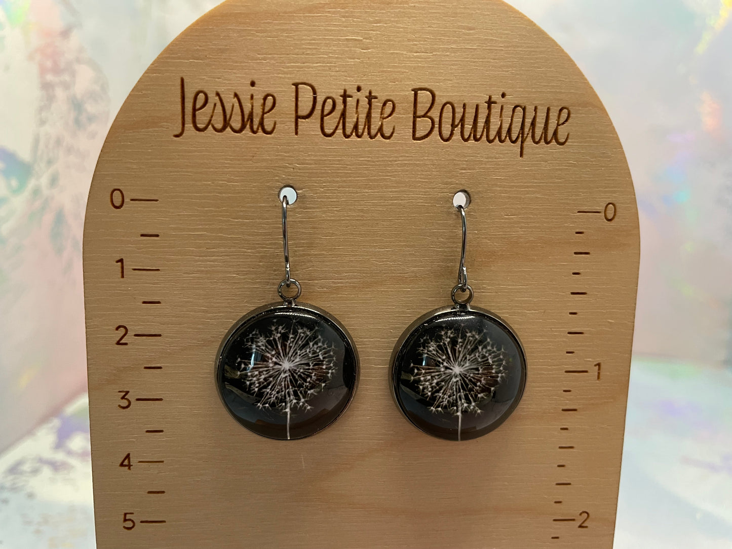 Dangle earrings with dandelion designs on a wooden card with 'Jessie Petite Boutique' branding.