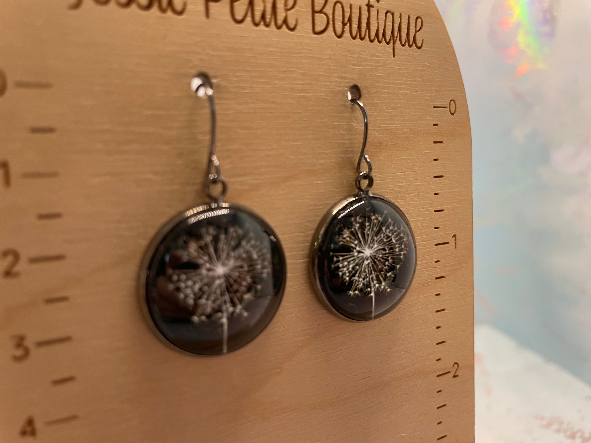 Dandelion seed earrings on a wooden card with measurement scale, branded 'JESSIE Petite Boutique'.