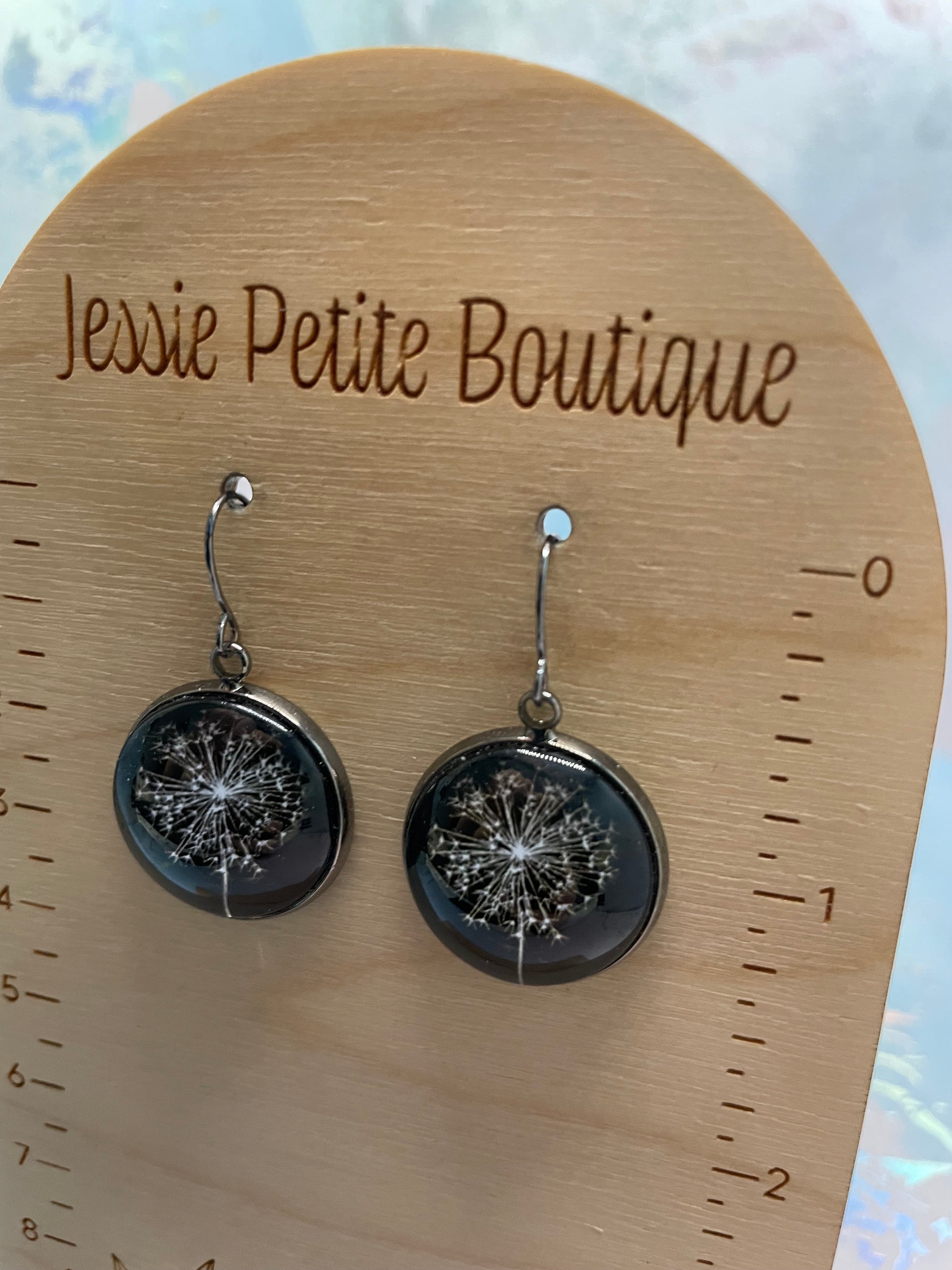 Pair of black and silver earrings on a wooden board with 'Jessie Petite Boutique' branding.