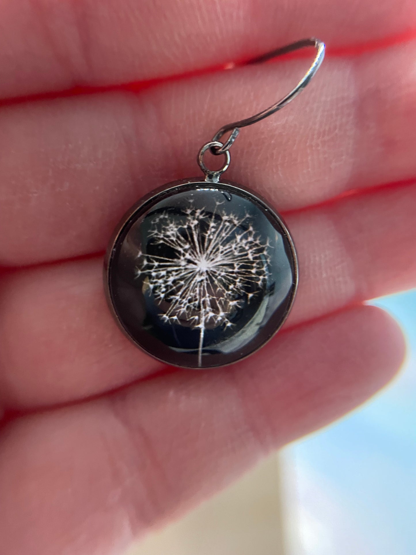 Earring with dandelion design held in a hand