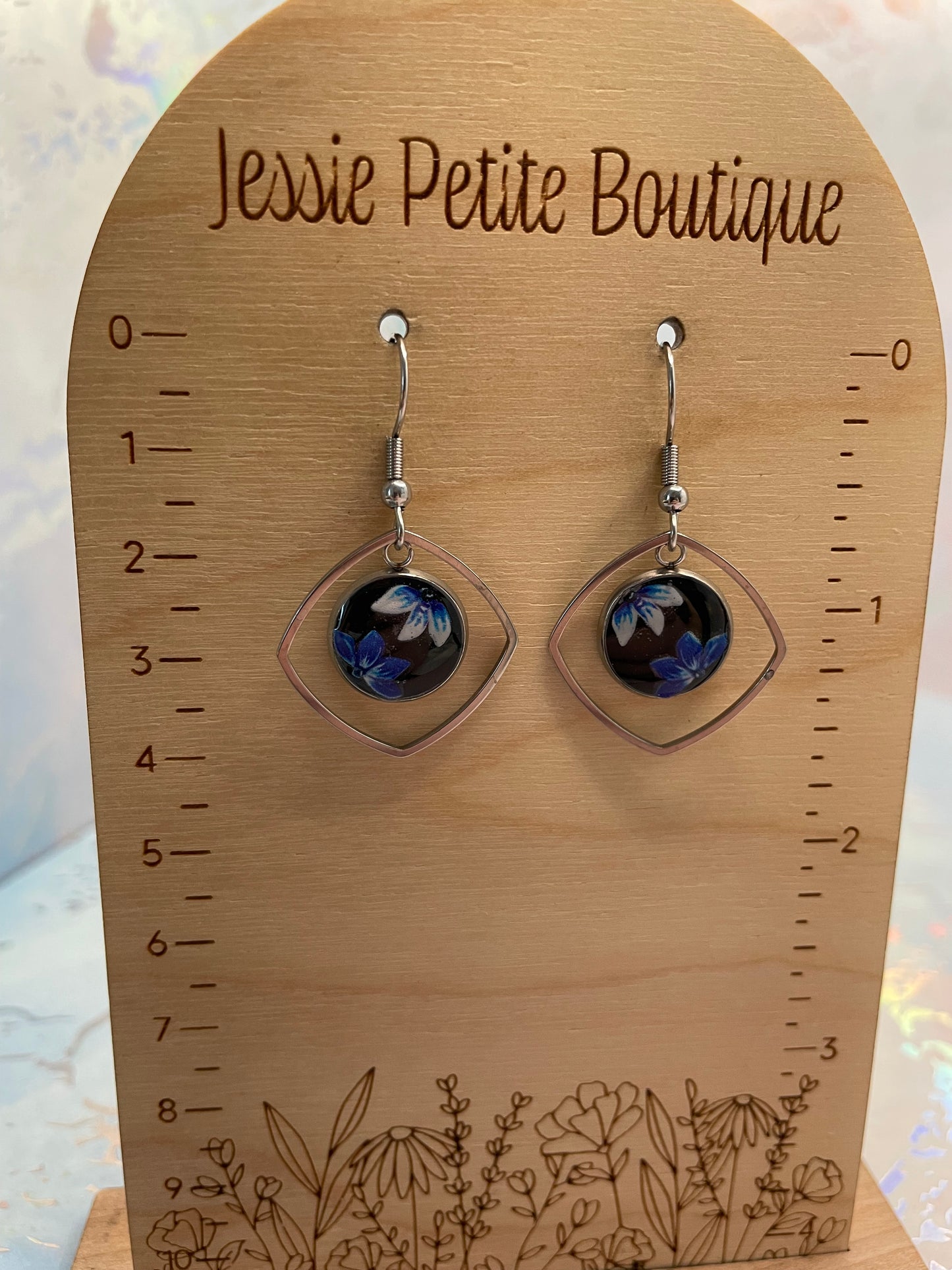 Pair of earrings on a wooden card with measurements and floral design, branded 'Jessie Petite Boutique'.