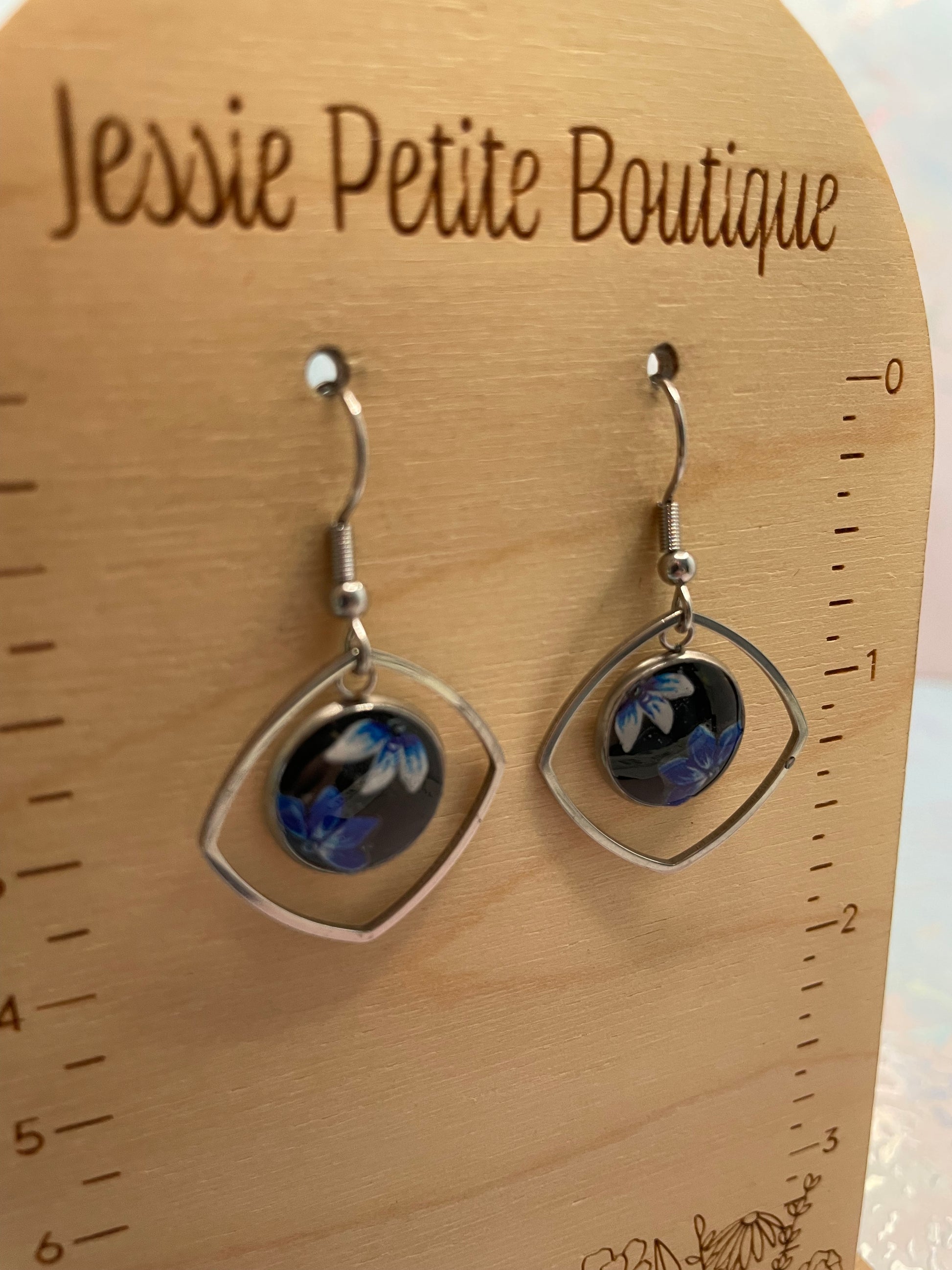 Pair of earrings on a wooden board with 'Jessie Petite Boutique' branding.