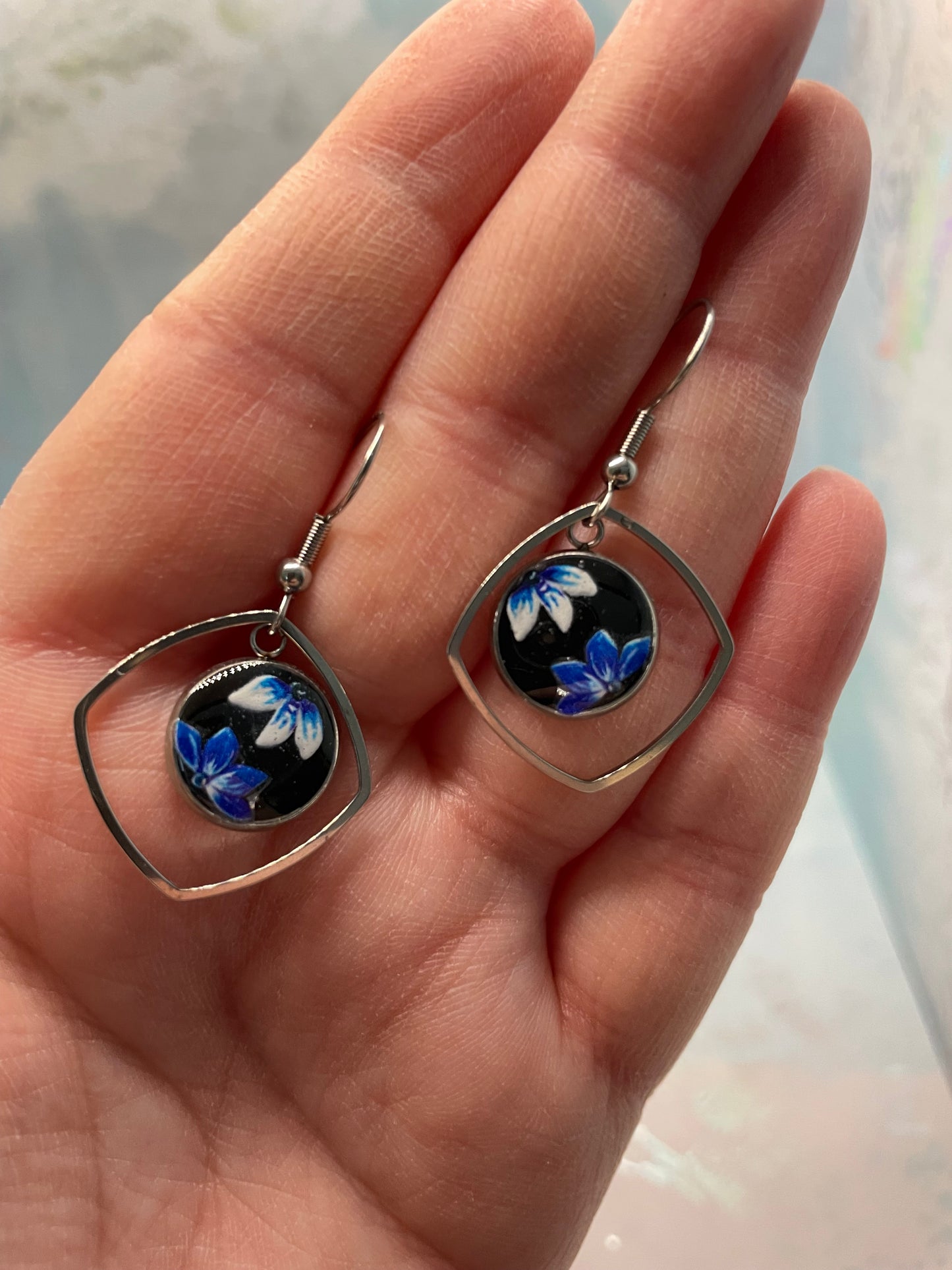 Hand holding a pair of floral earrings with a blurred background