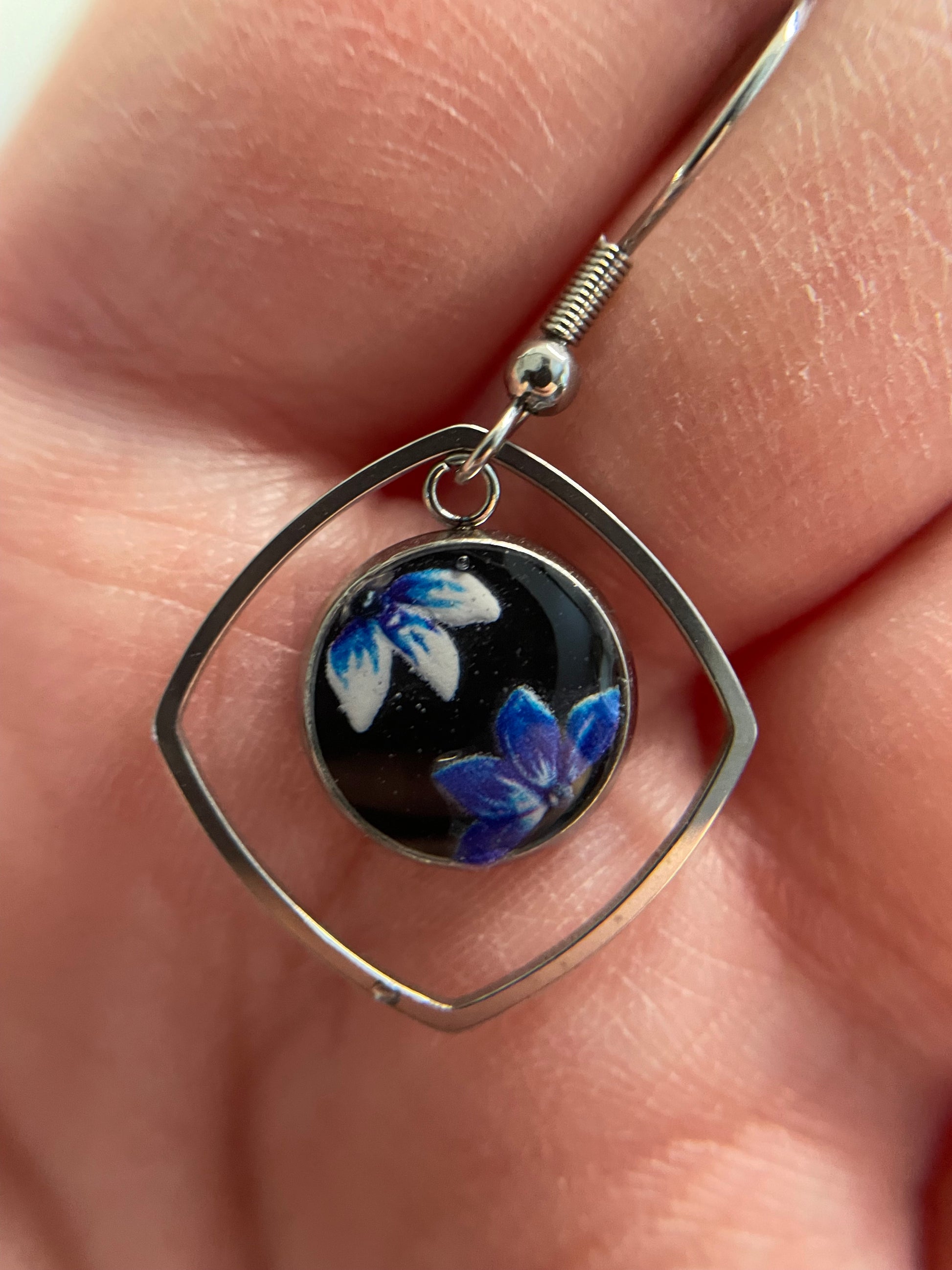 Silver earring with floral design on a black background held between fingers.