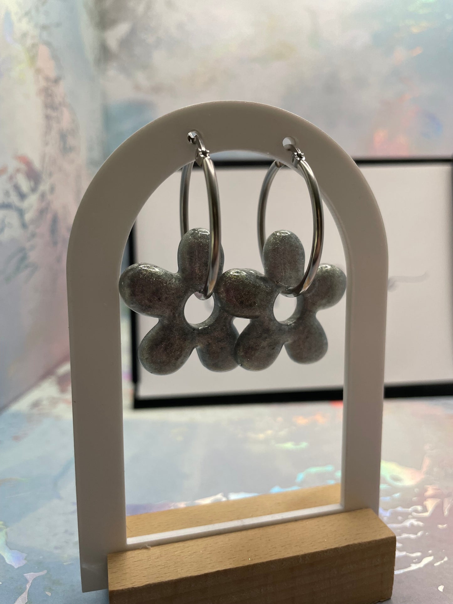 Silver flower-shaped earrings on a white stand with a blurred background