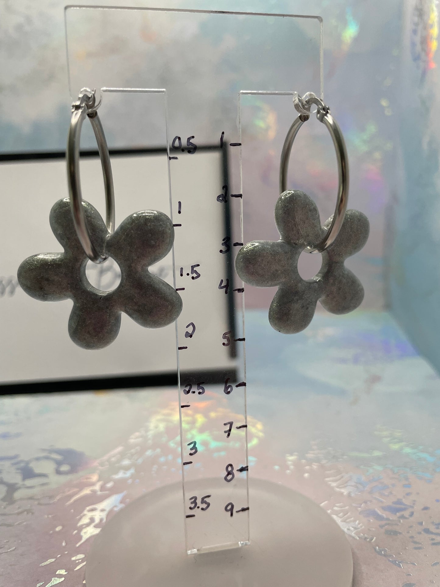 Flower-shaped earrings on a clear stand with measurement scale