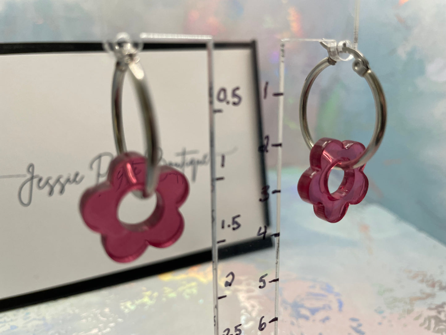 Silver hoop earrings with pink flower charms on a clear stand with measurement scale.