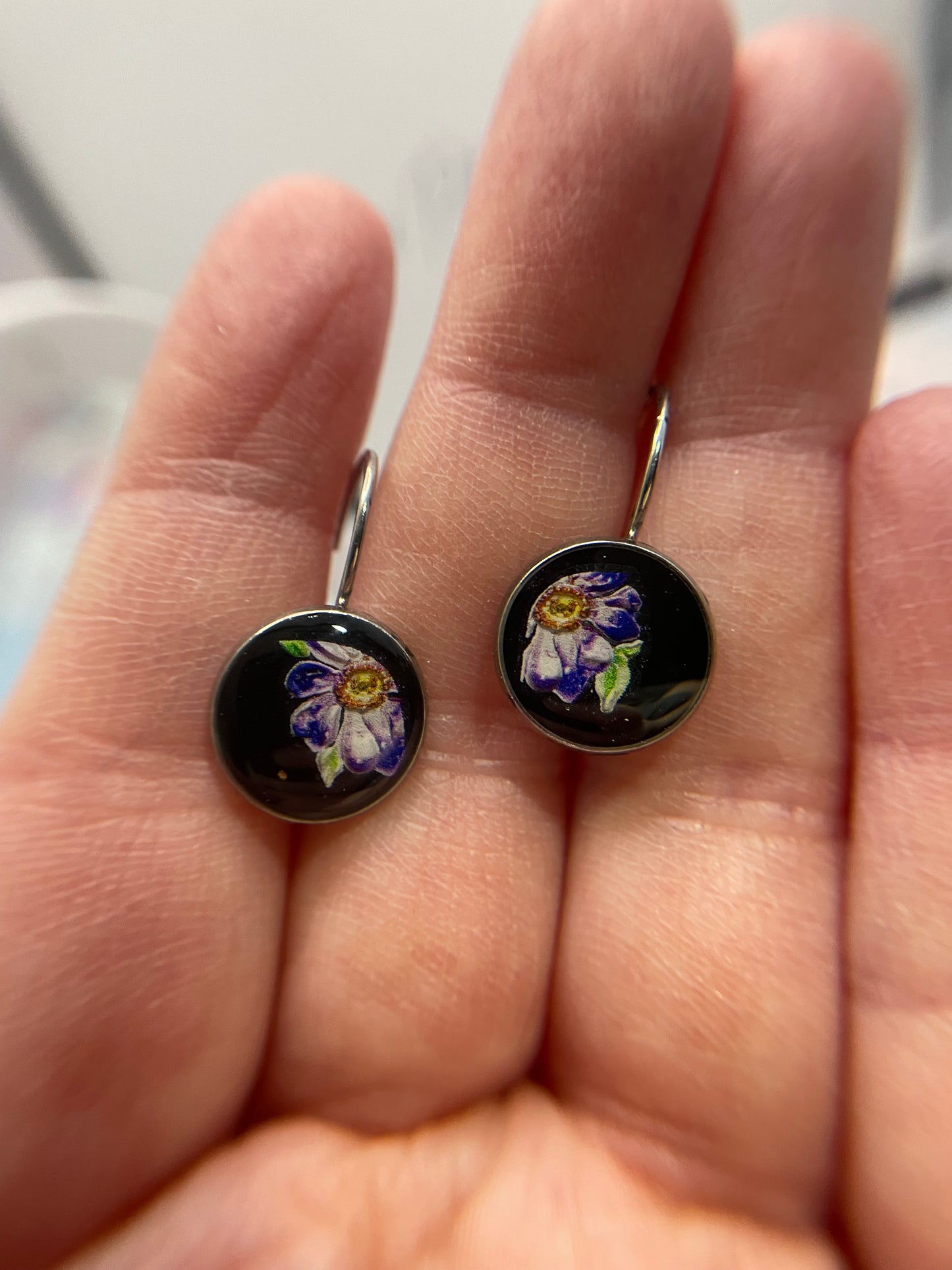 Pair of floral earrings held in a hand with a blurred background