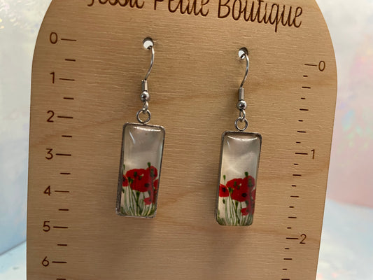Rectangular earrings with red floral design on a wooden measurement card.