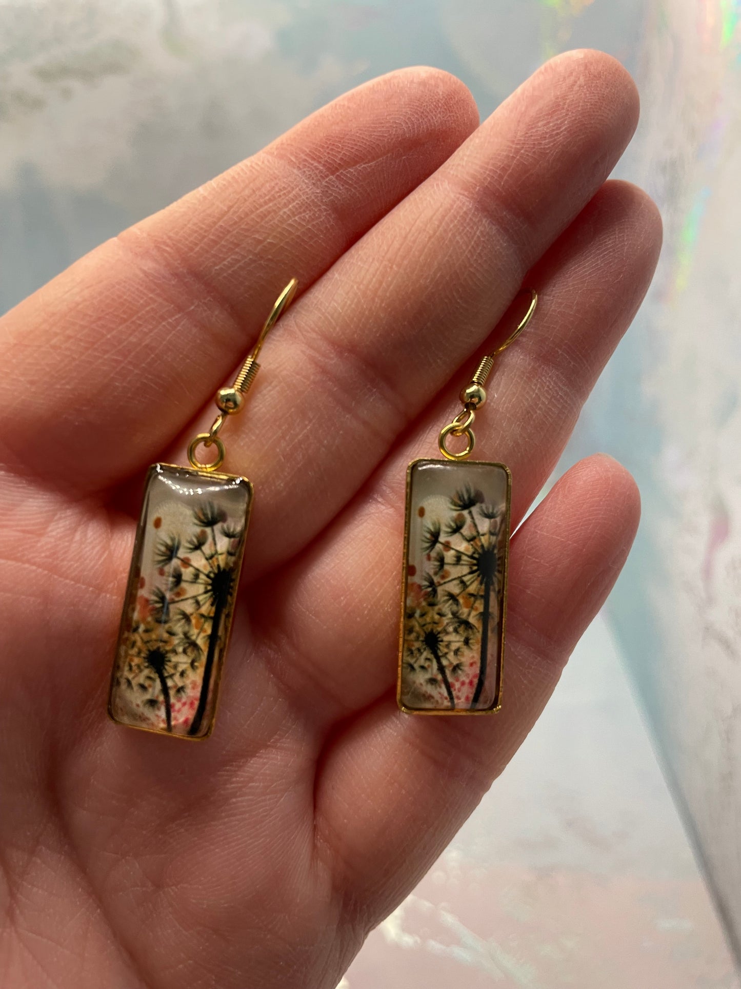 Gold earrings with floral design held in a hand against a light background