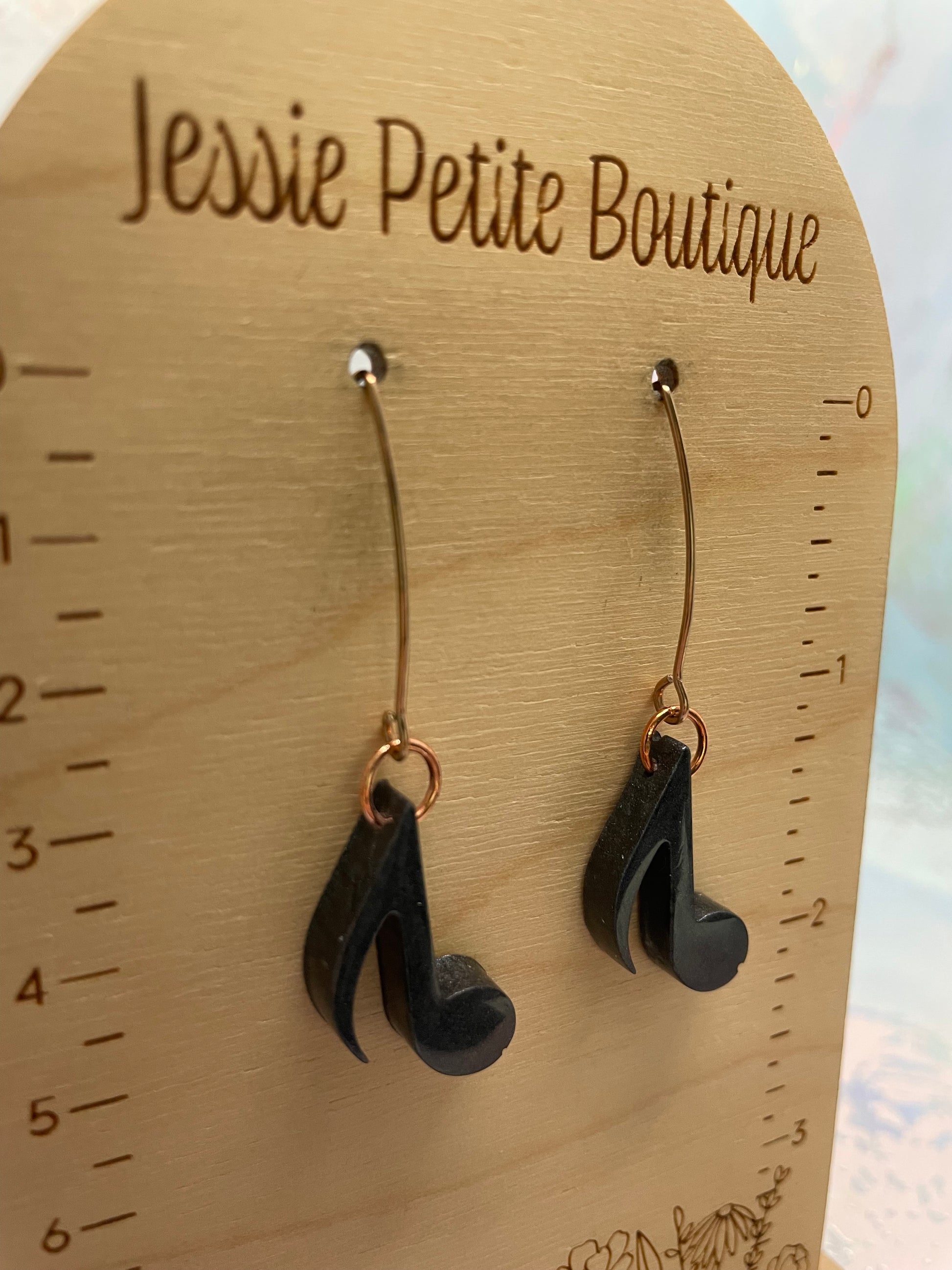 Black music note earrings on a wooden board with 'Jessie Petite Boutique' branding.