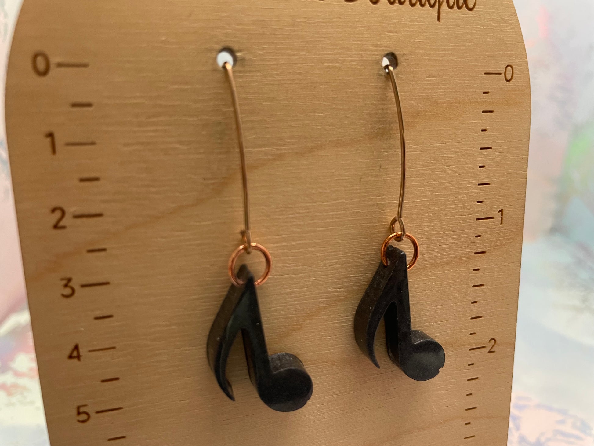 Black music note earrings on a wooden display card with measurements.