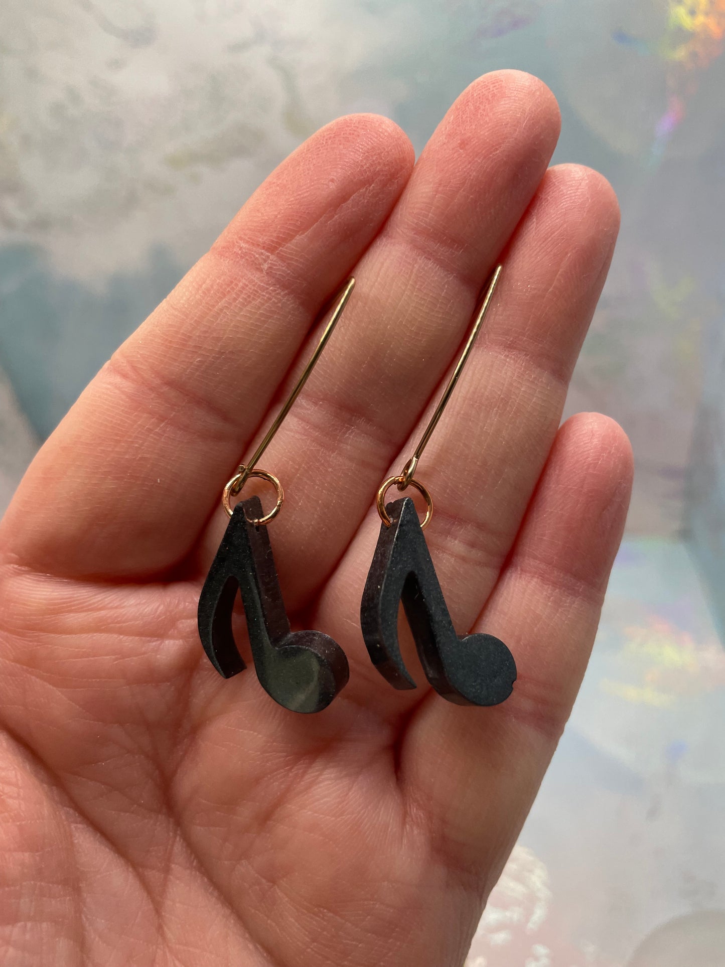 Black music note earrings held in a hand with a blurred background
