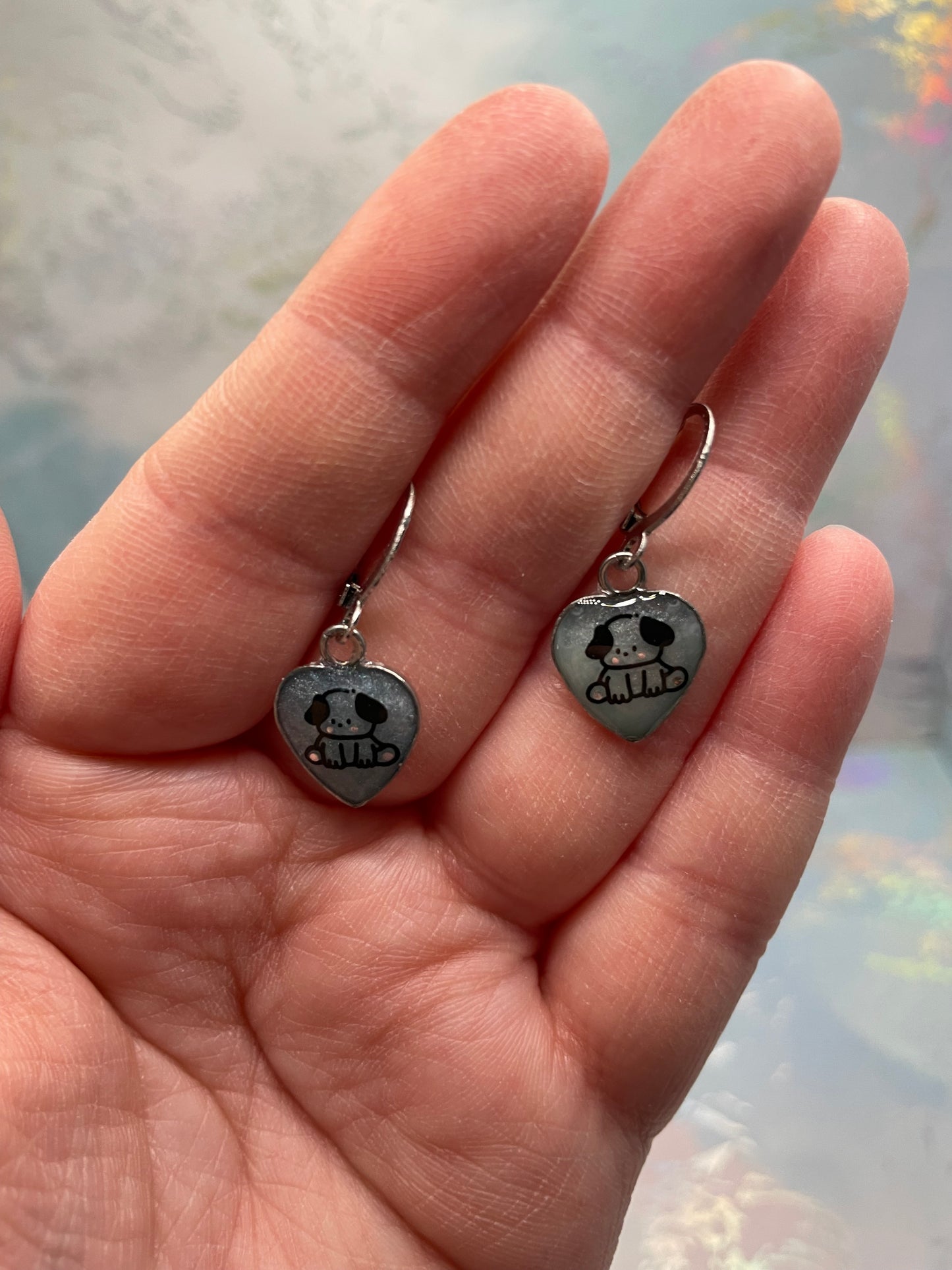 Heart-shaped earrings with skull designs held between fingers against a blurred background