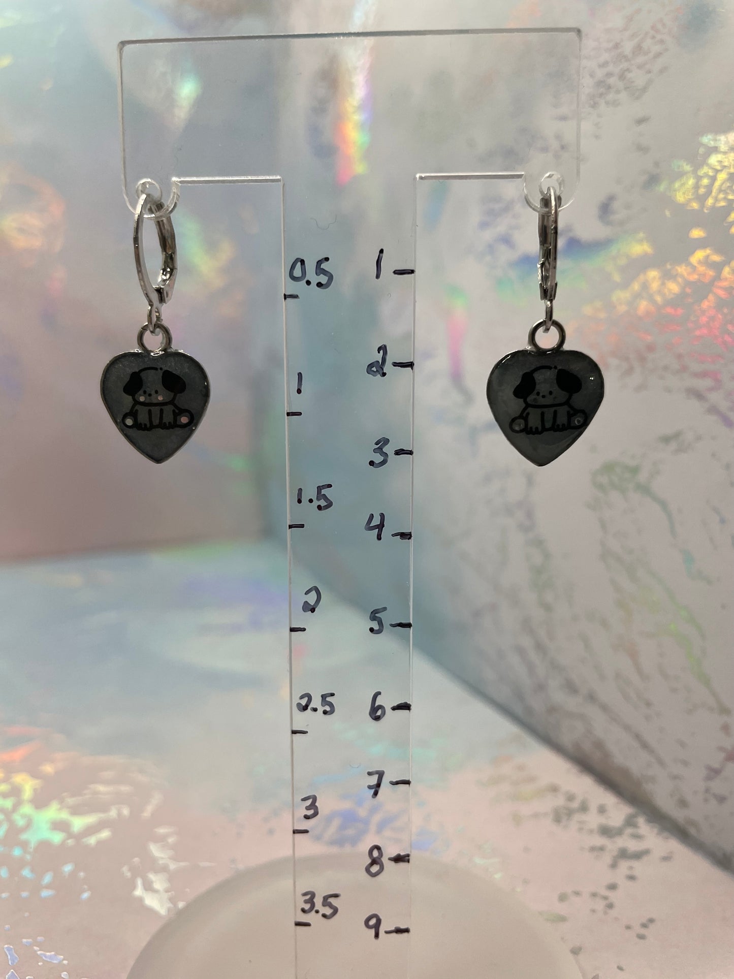 Cute Puppy Heart Dangle Earrings on a clear card with measurements against a colorful, blurred background.