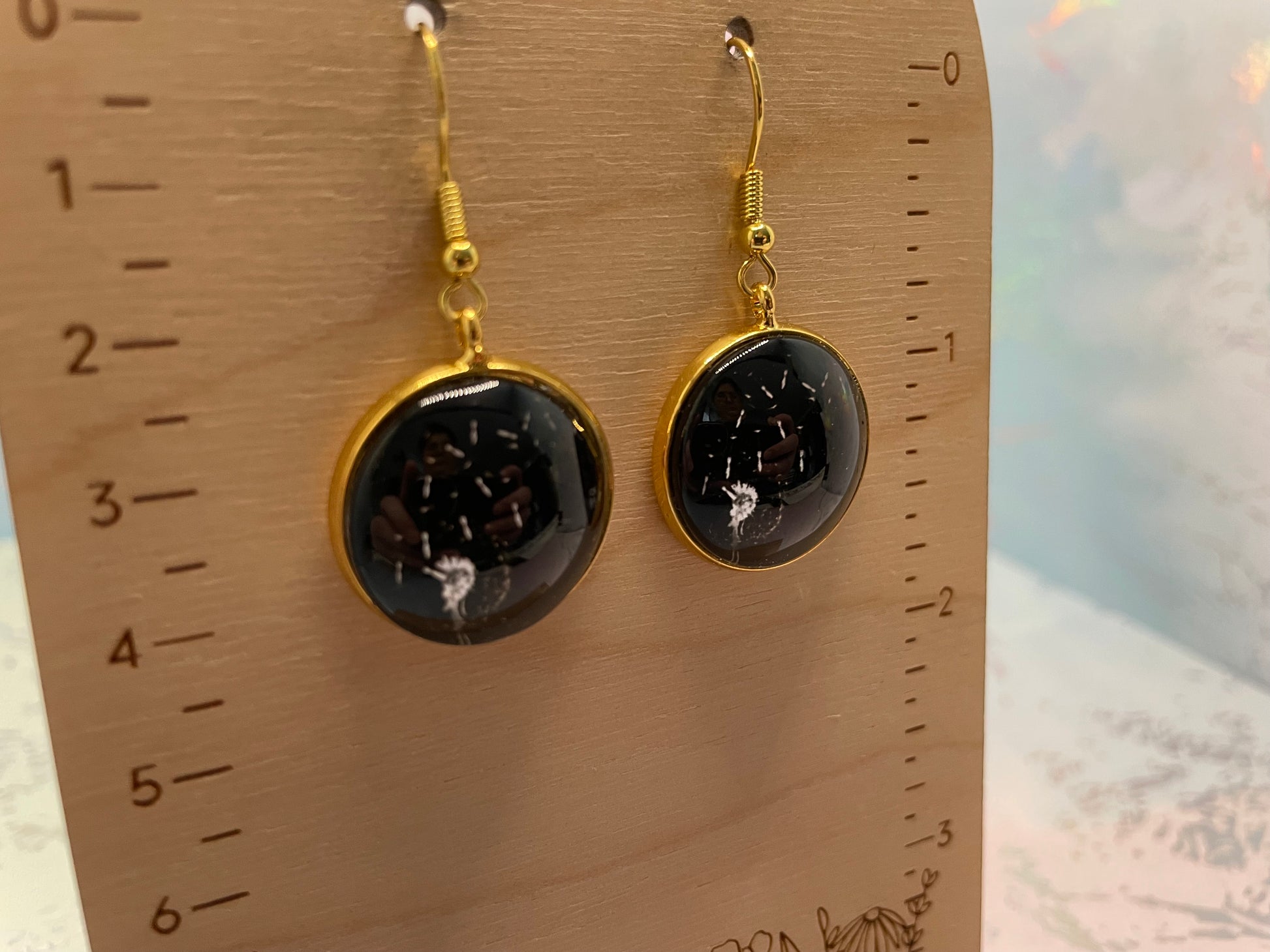 Gold-framed Dandelion Round Cabochon Earrings on a wooden ruler