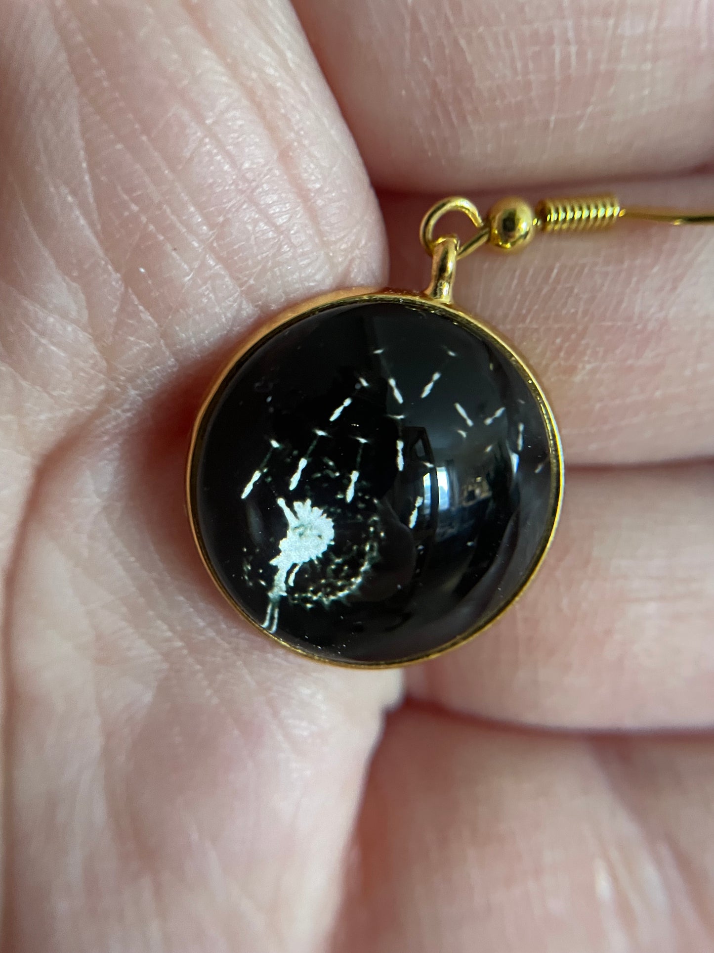 Dandelion Round Cabochon Earrings with gold setting on a finger
