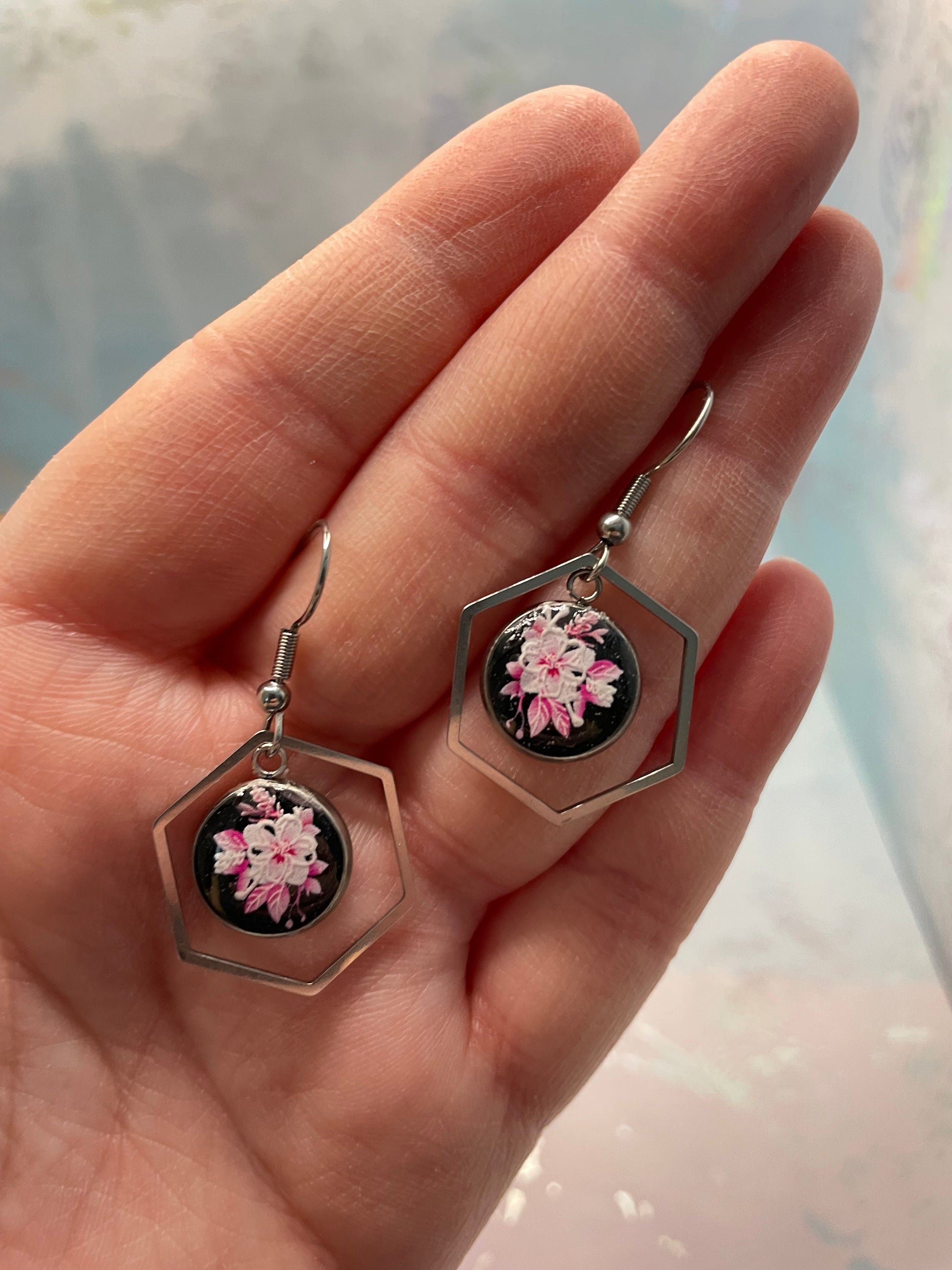 Hexagonal earrings with floral design held in a hand against a light background