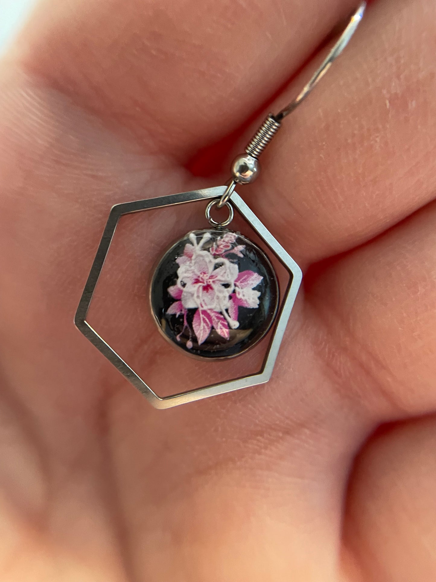 Hexagonal earrings with floral design held in a hand