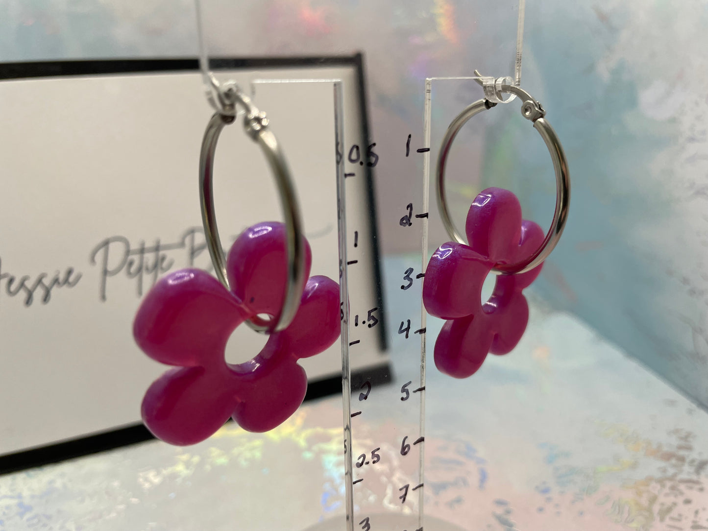 Pink flower-shaped earrings on a clear stand with a blurred background