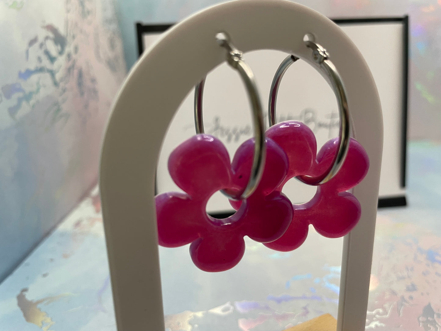 Pink flower-shaped earrings on a white stand with a blurred background